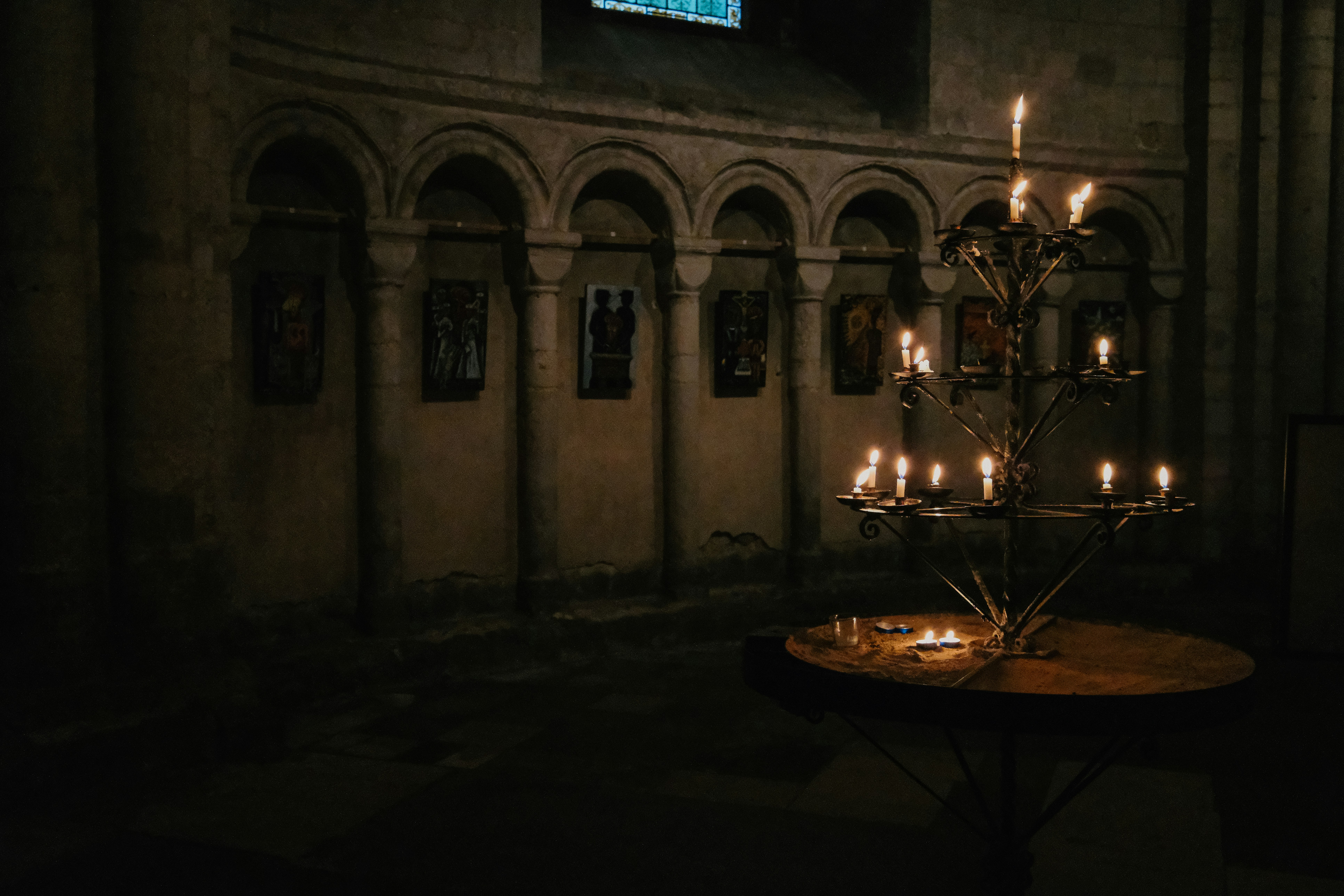 A tiered metal candle stand with lit candles in a dim stone church