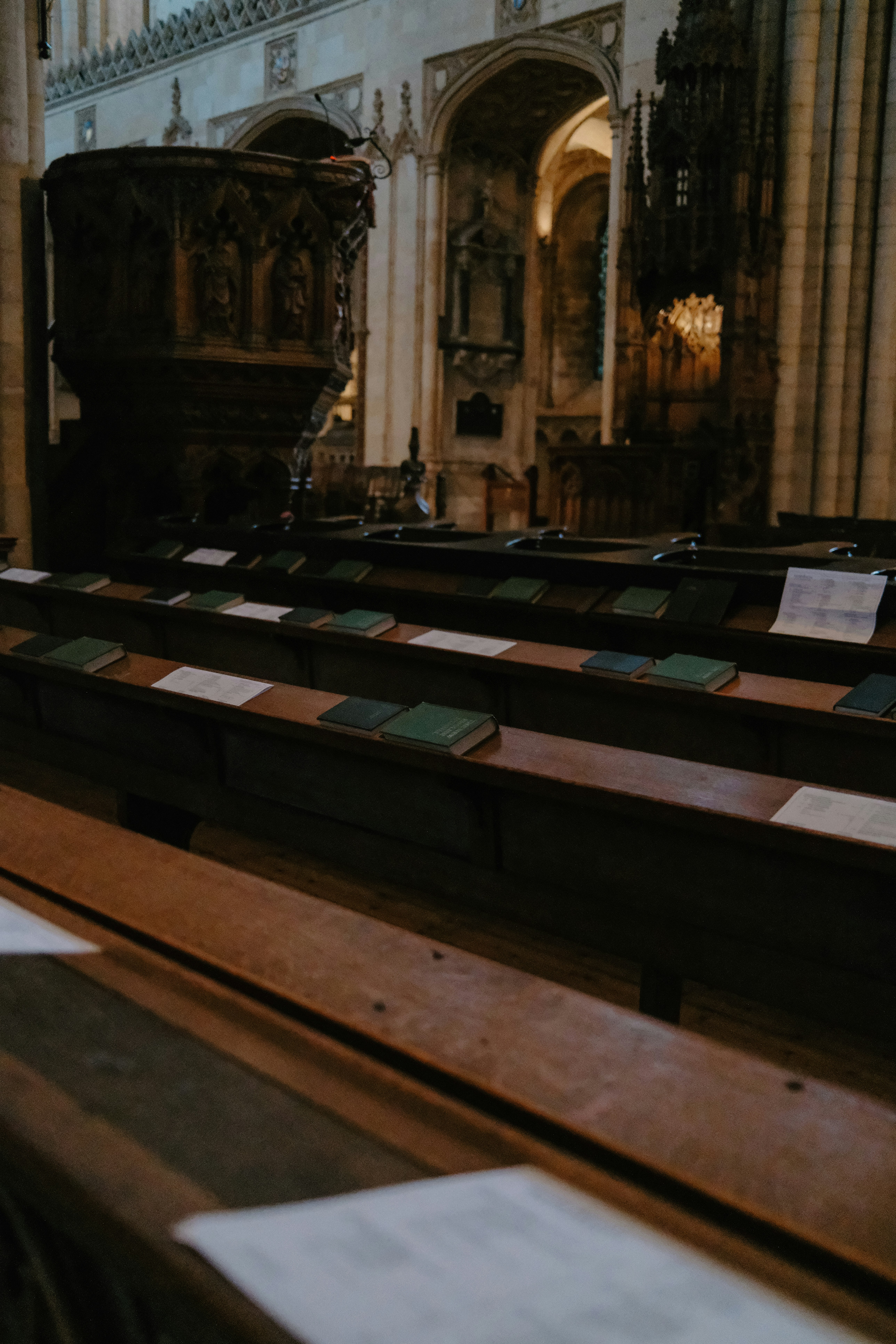 Wooden pews with green books and white papers inside a stone cathedral