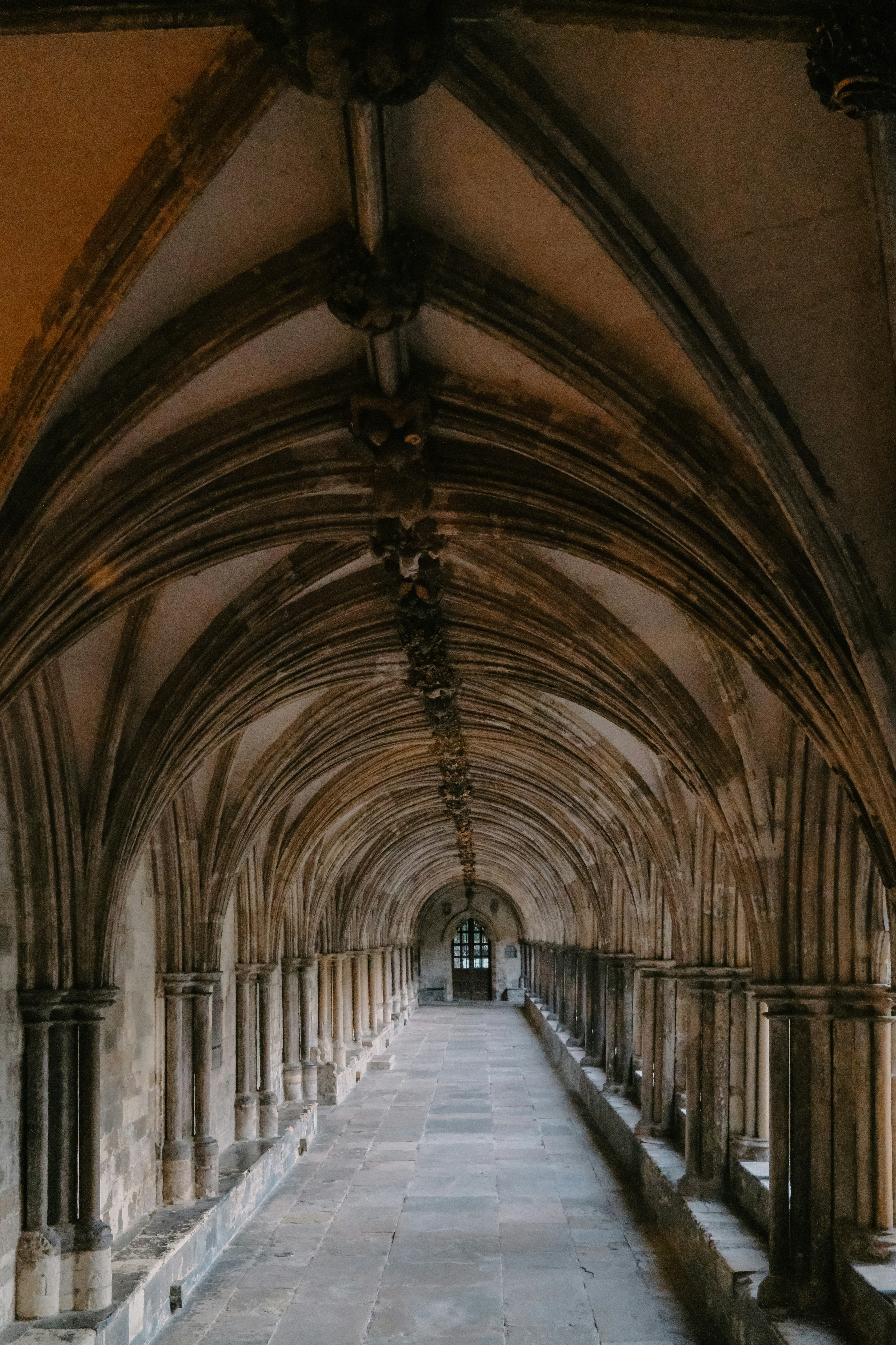 A stone cloister with vaulted ceilings and columns leading to a distant doorway