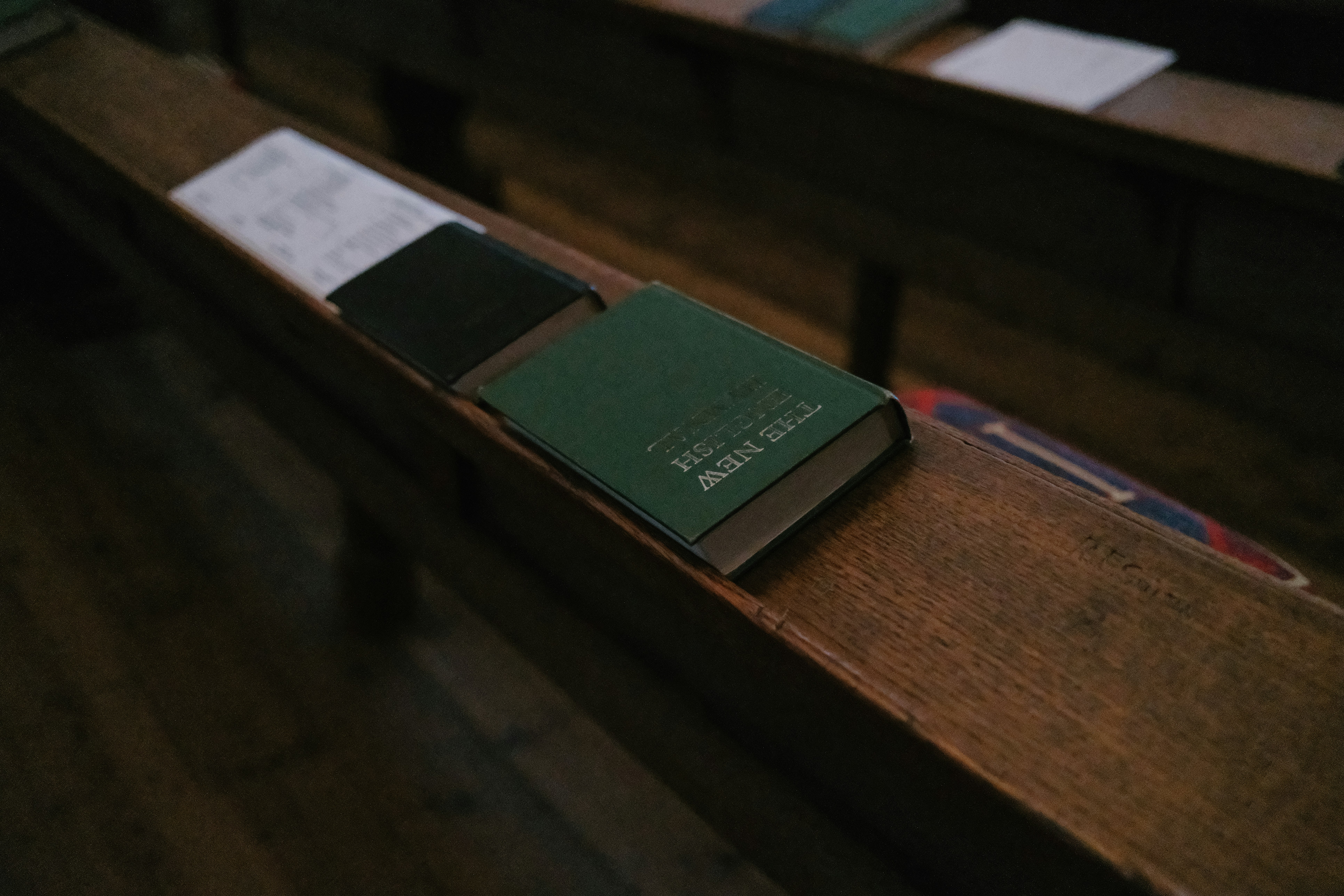 A green book and a black book on a wooden church pew