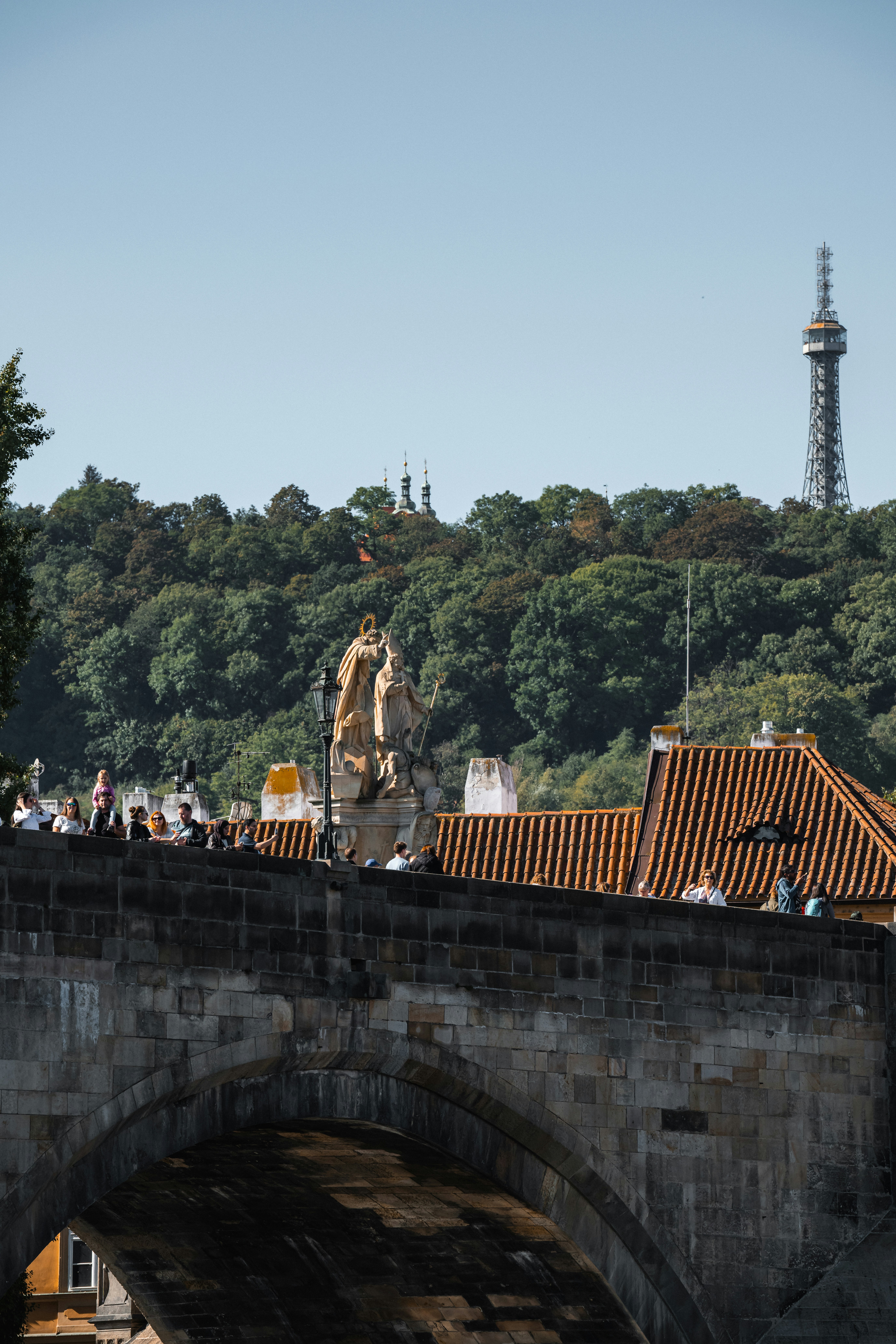 People walking on the stone Charles Bridge in Prague with Petrin Tower in background