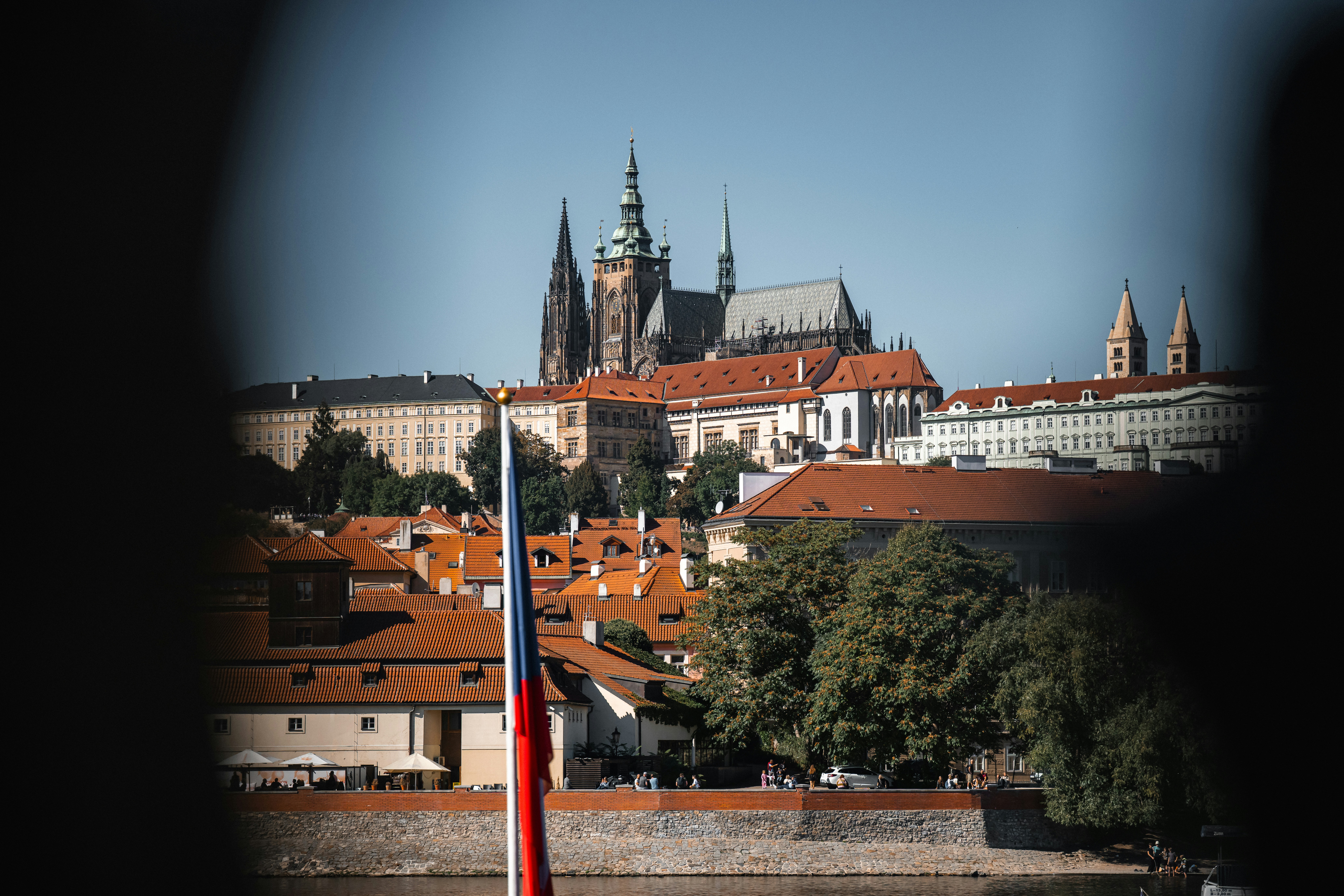 St. Vitus Cathedral rising above red-tiled roofs in Prague with a flag in foreground