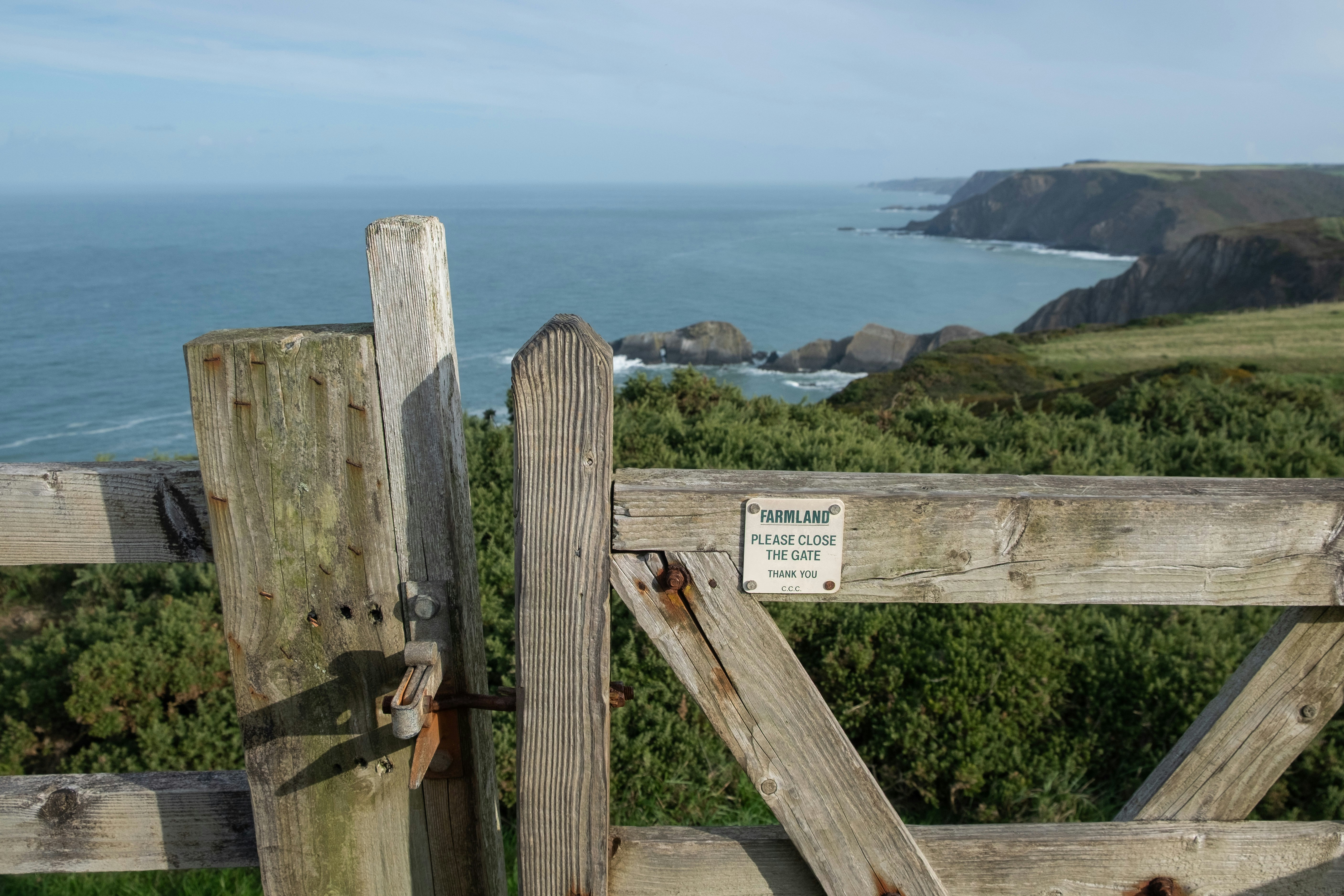 A wooden gate with a sign reading "PLEASE CLOSE THE GATE" overlooking the ocean