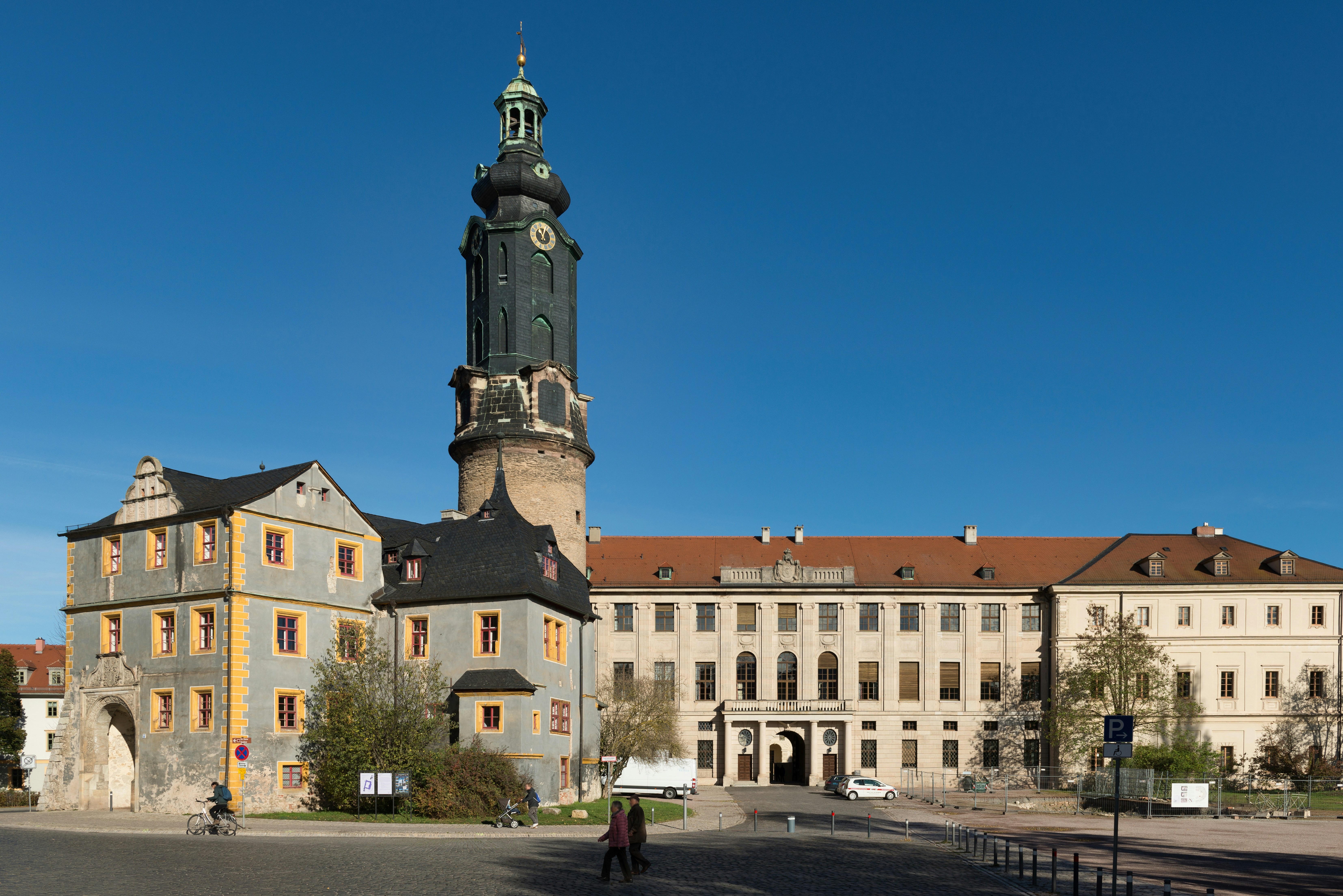 A tall clock tower and historic buildings in a town square under clear blue sky