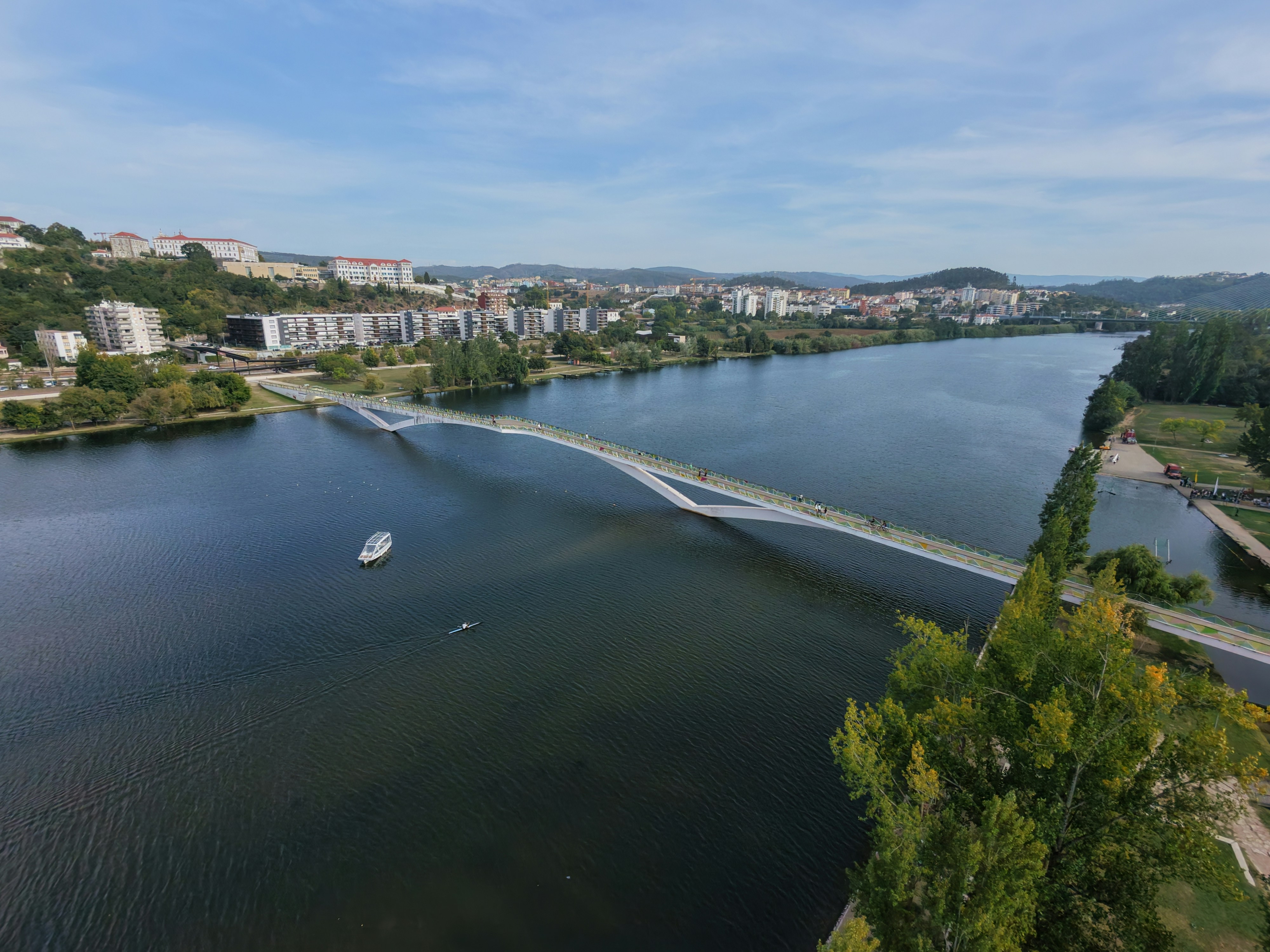 A white pedestrian bridge spanning a wide river with a city in the background