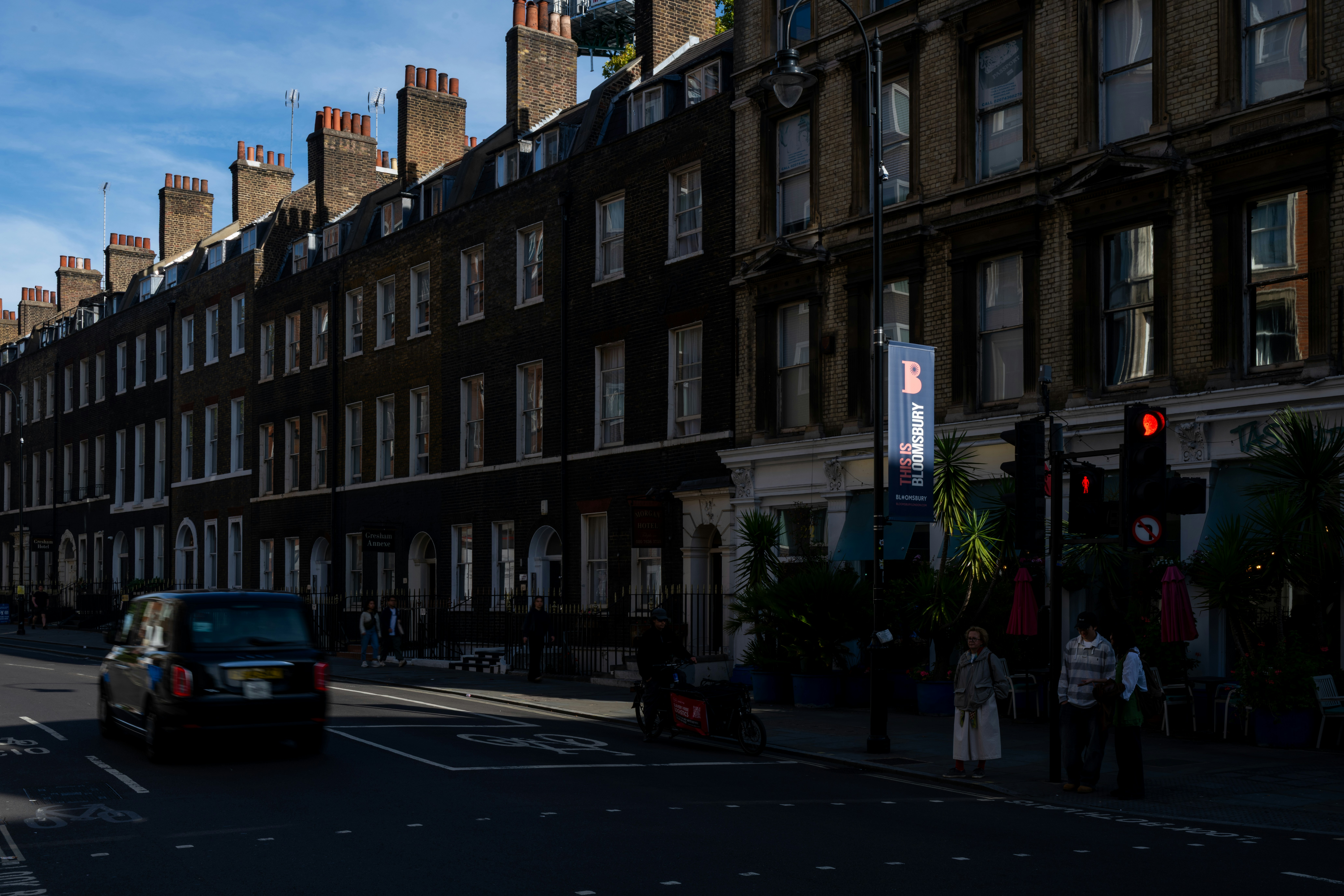 A black taxi driving past brick buildings on a street in Bloomsbury, London
