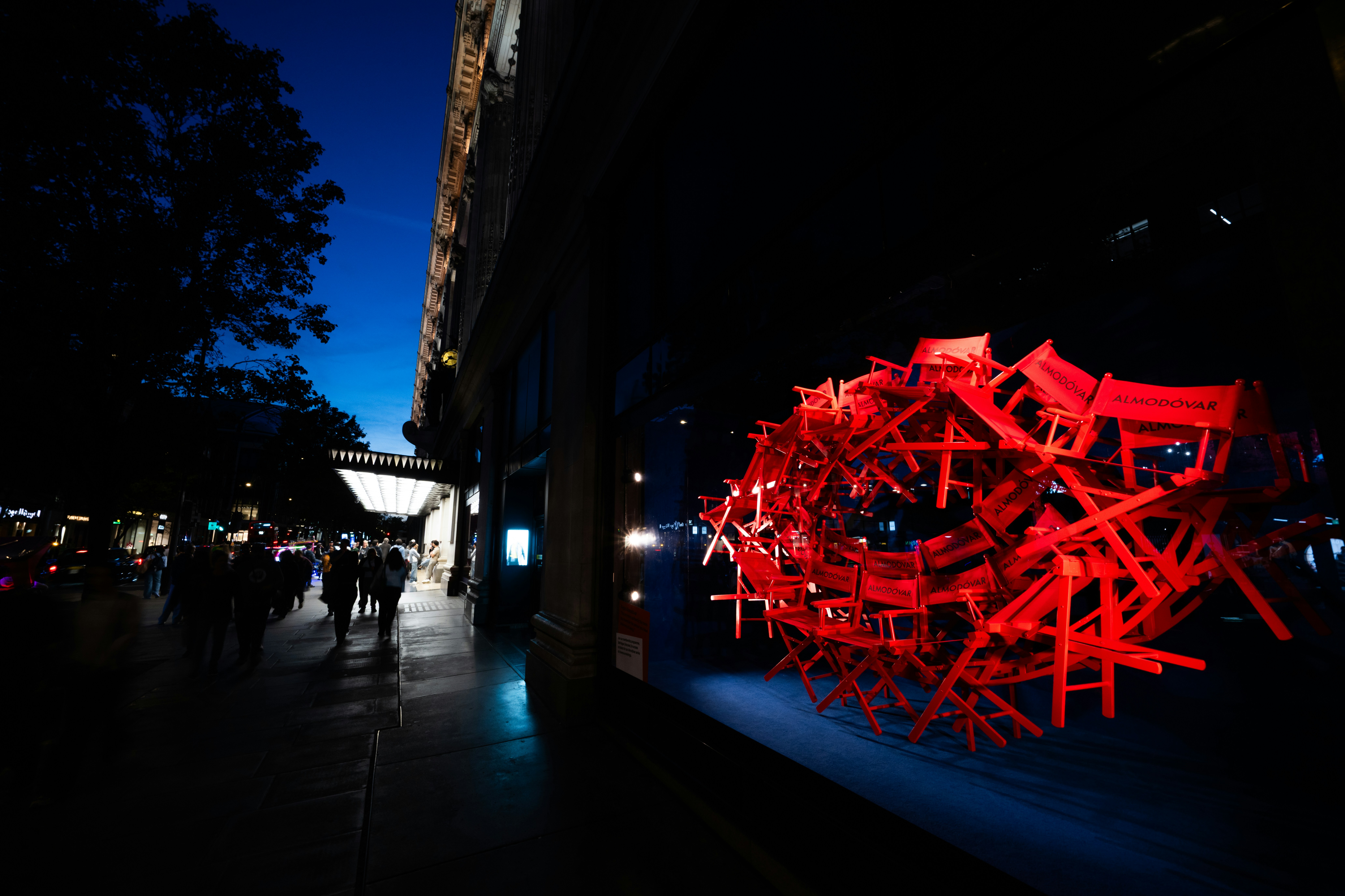 A circular sculpture of red director chairs in a brightly lit storefront window at night