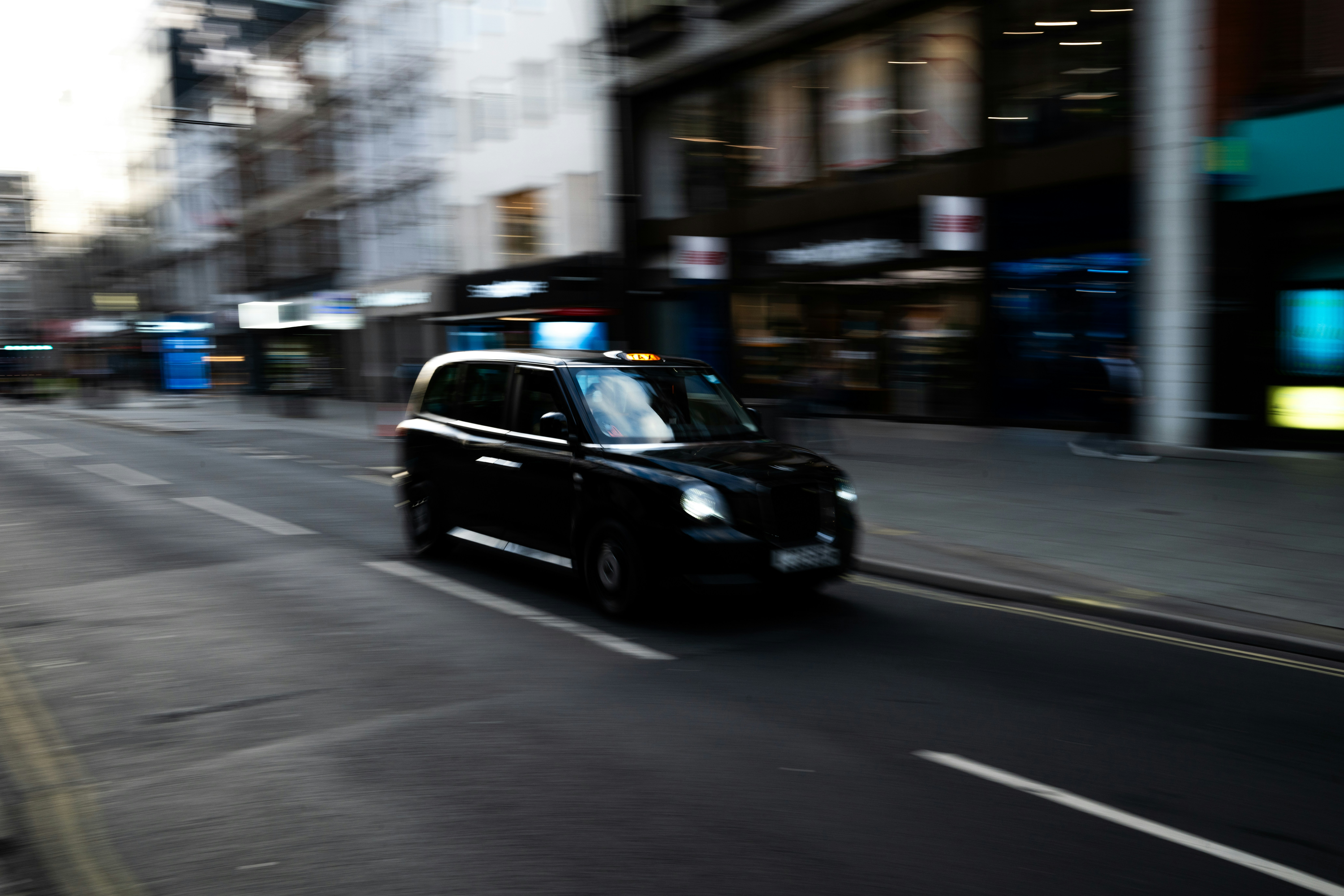 A black London taxi driving along a city street with motion blur