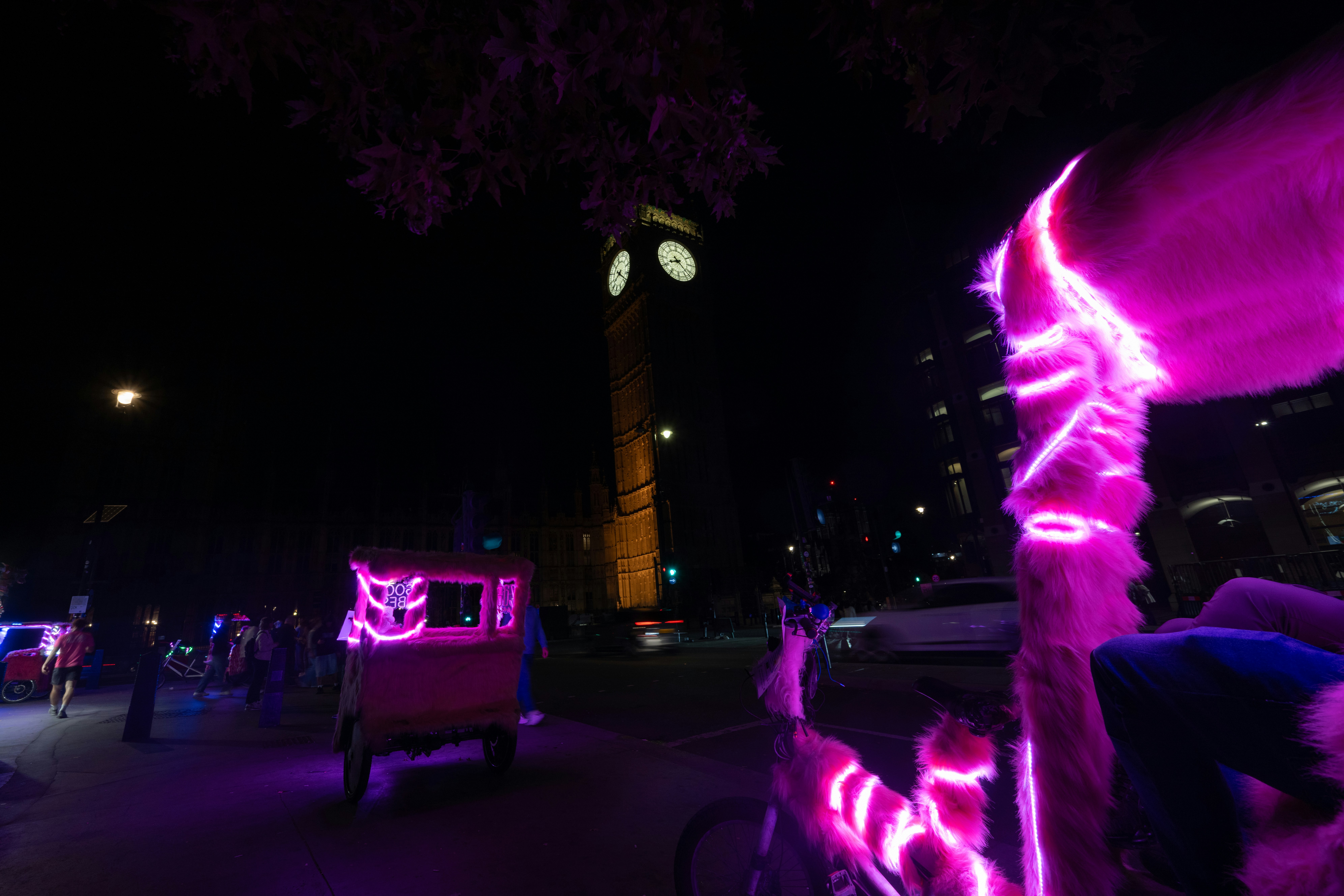 Pink neon-lit pedicabs with furry covers near Big Ben in London at night