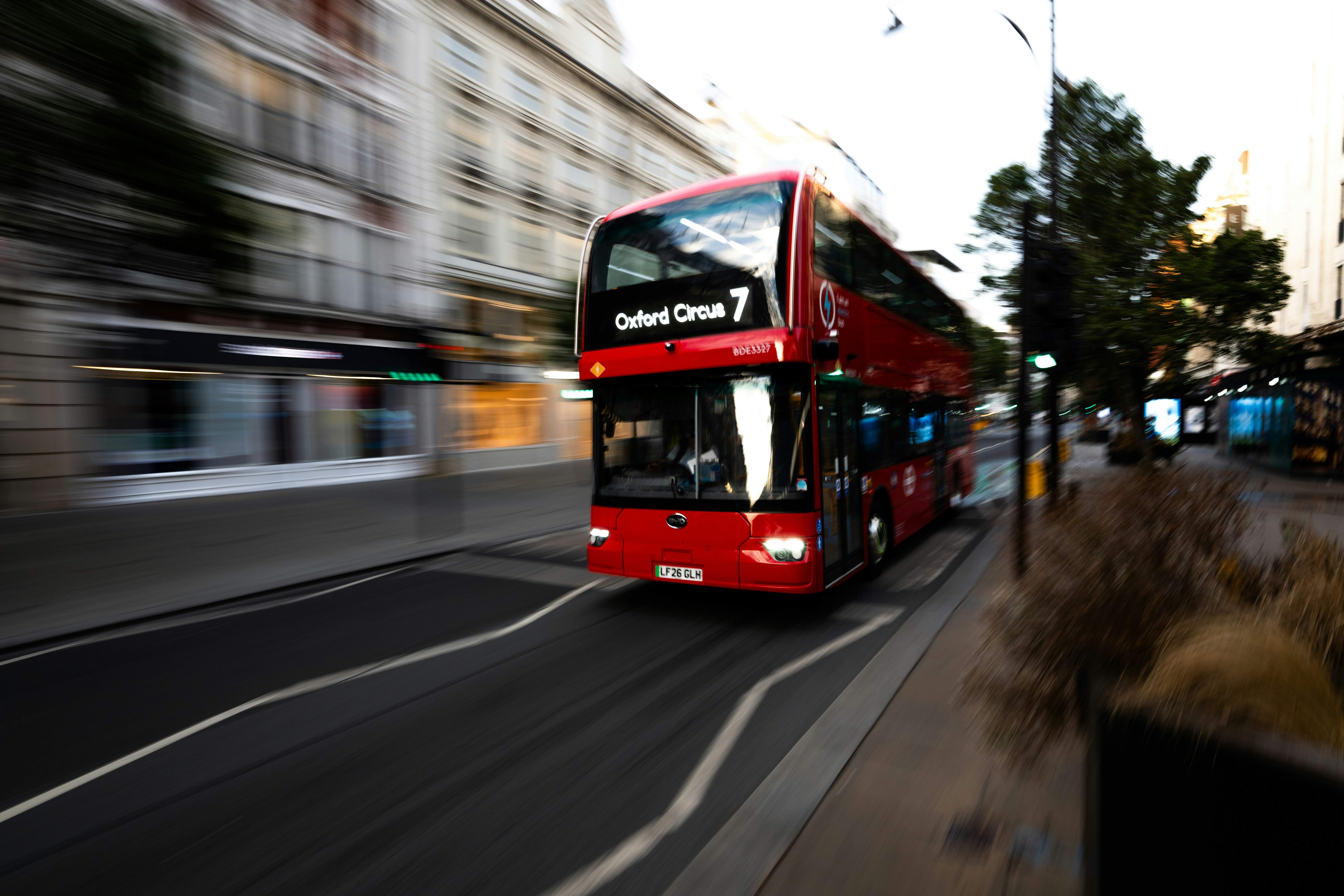 A red double-decker bus moving along a street in London with motion blur