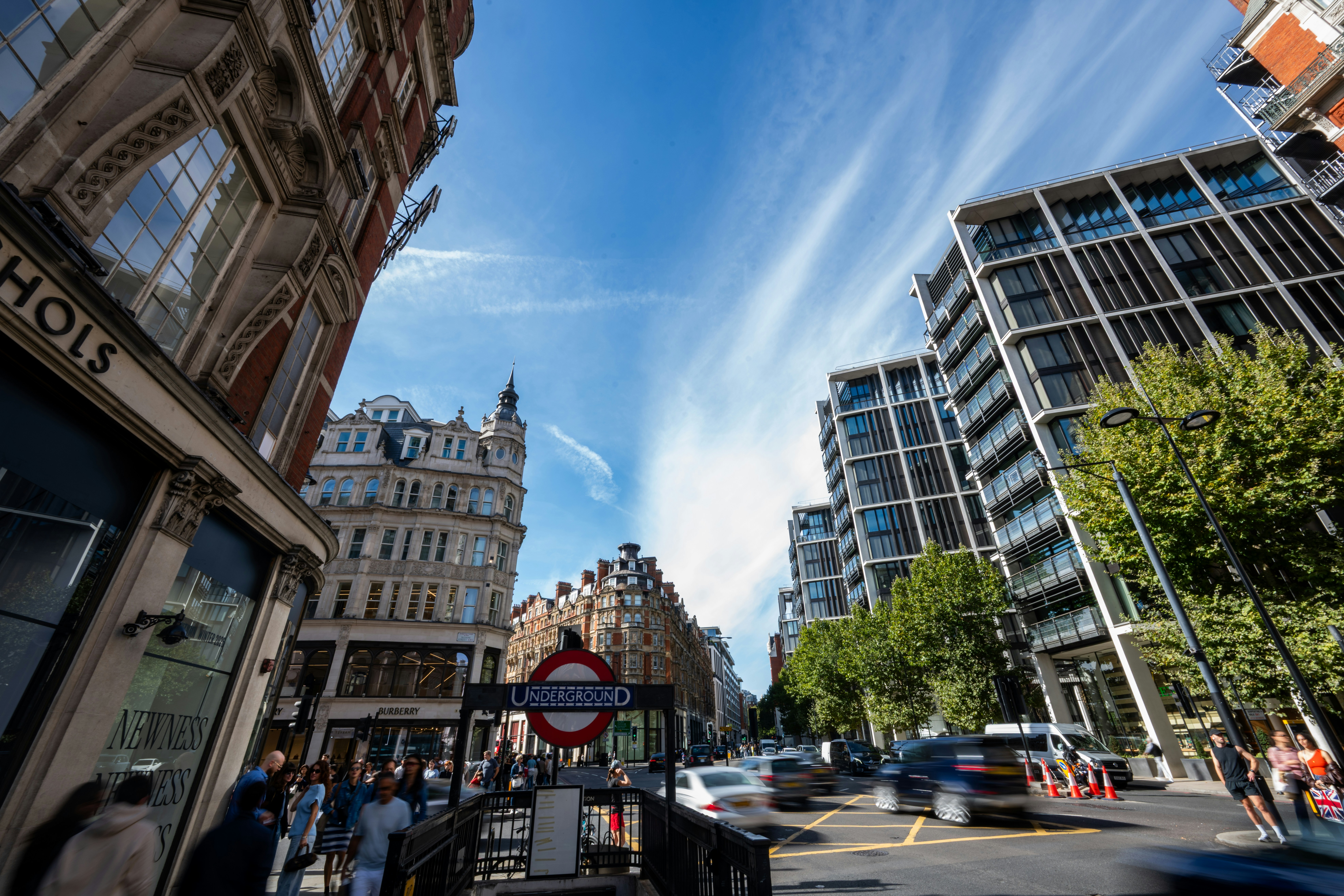 A London Underground sign above a busy street with historic and modern buildings