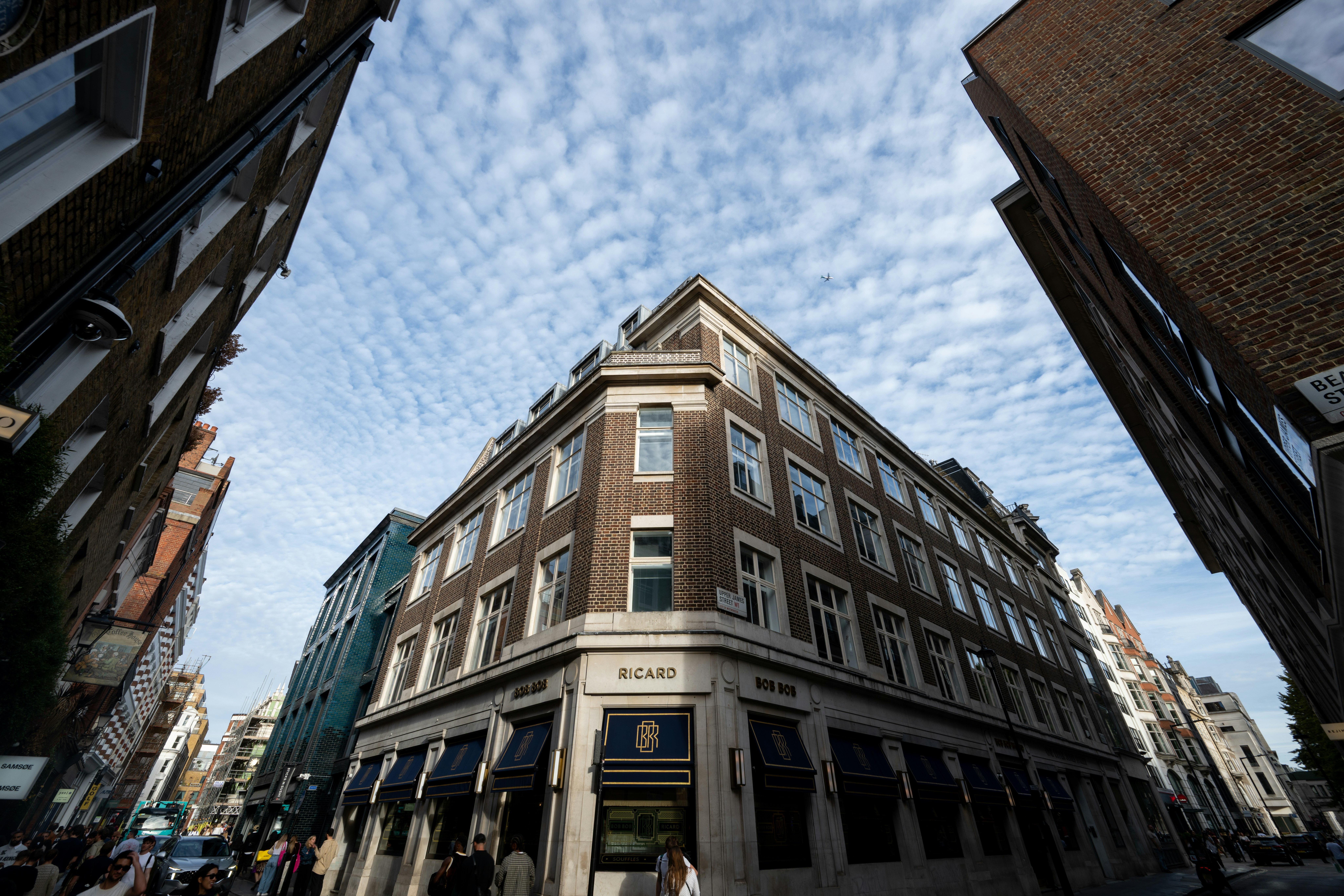 A corner brick building with blue awnings under a sky with scattered clouds