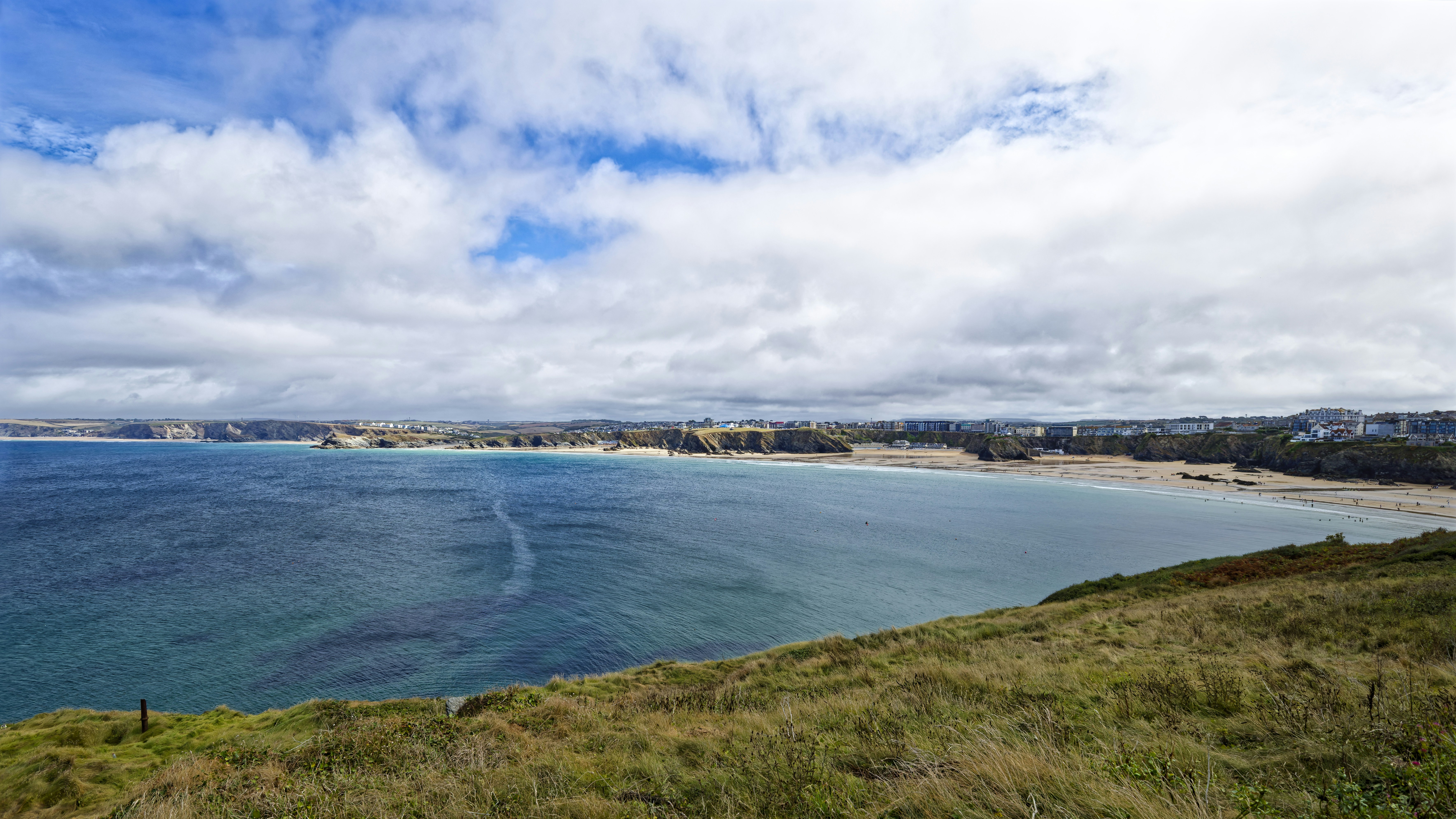 A sandy beach and blue ocean under a cloudy sky in Newquay