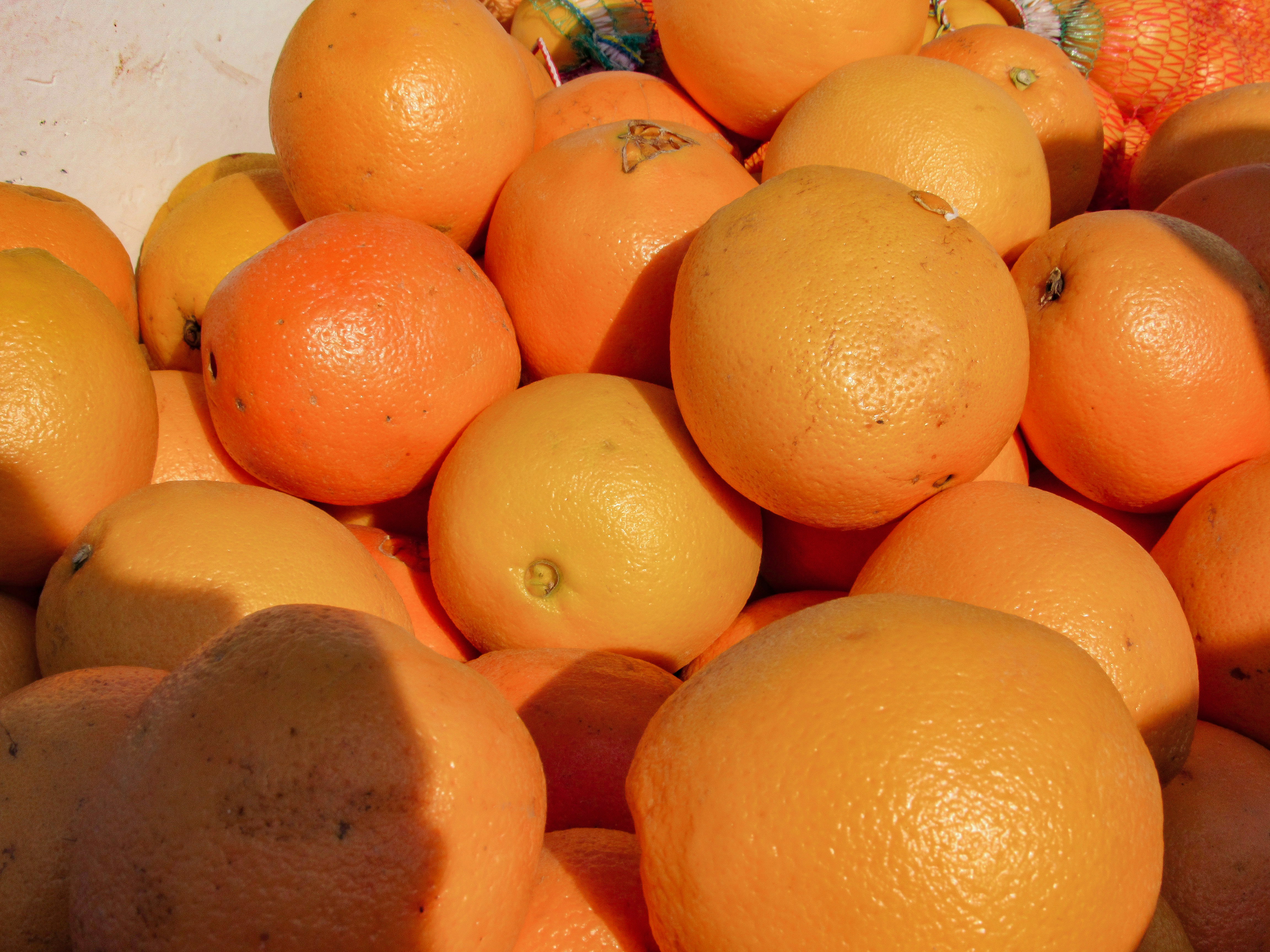 A pile of fresh oranges with textured rinds in bright sunlight