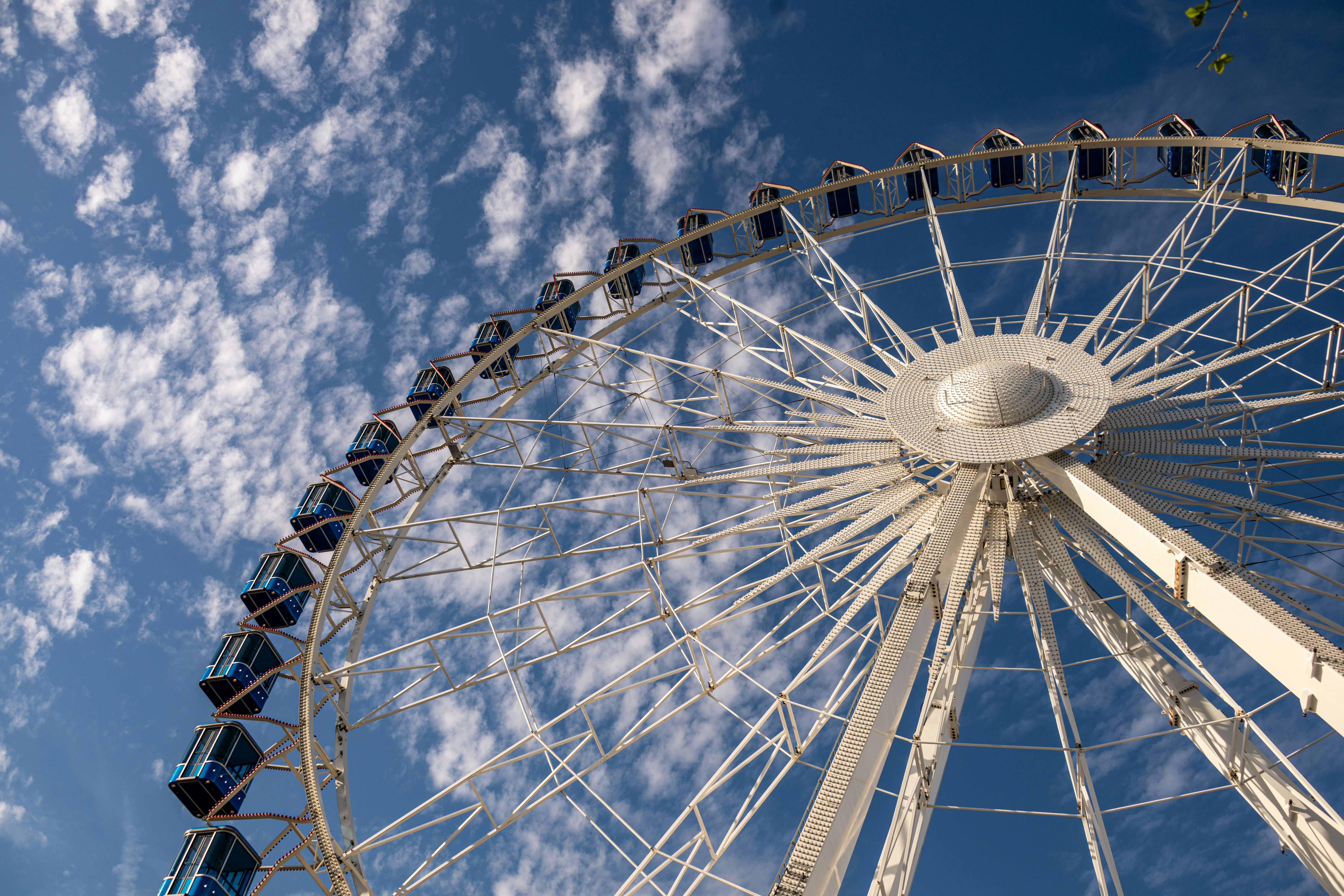A large white ferris wheel with blue passenger cars against a cloudy blue sky