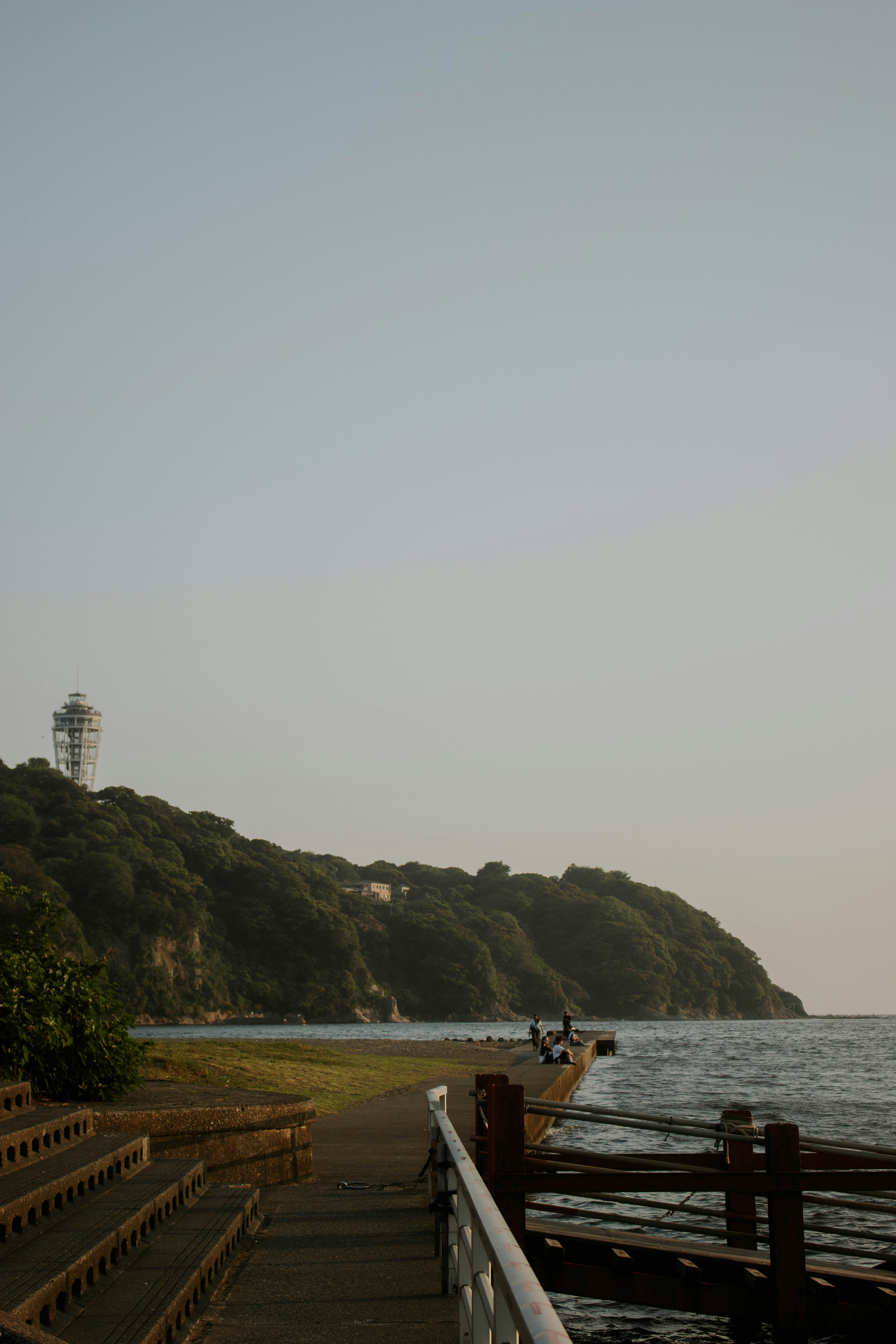 A concrete path along the coast with a forested hill and observation tower