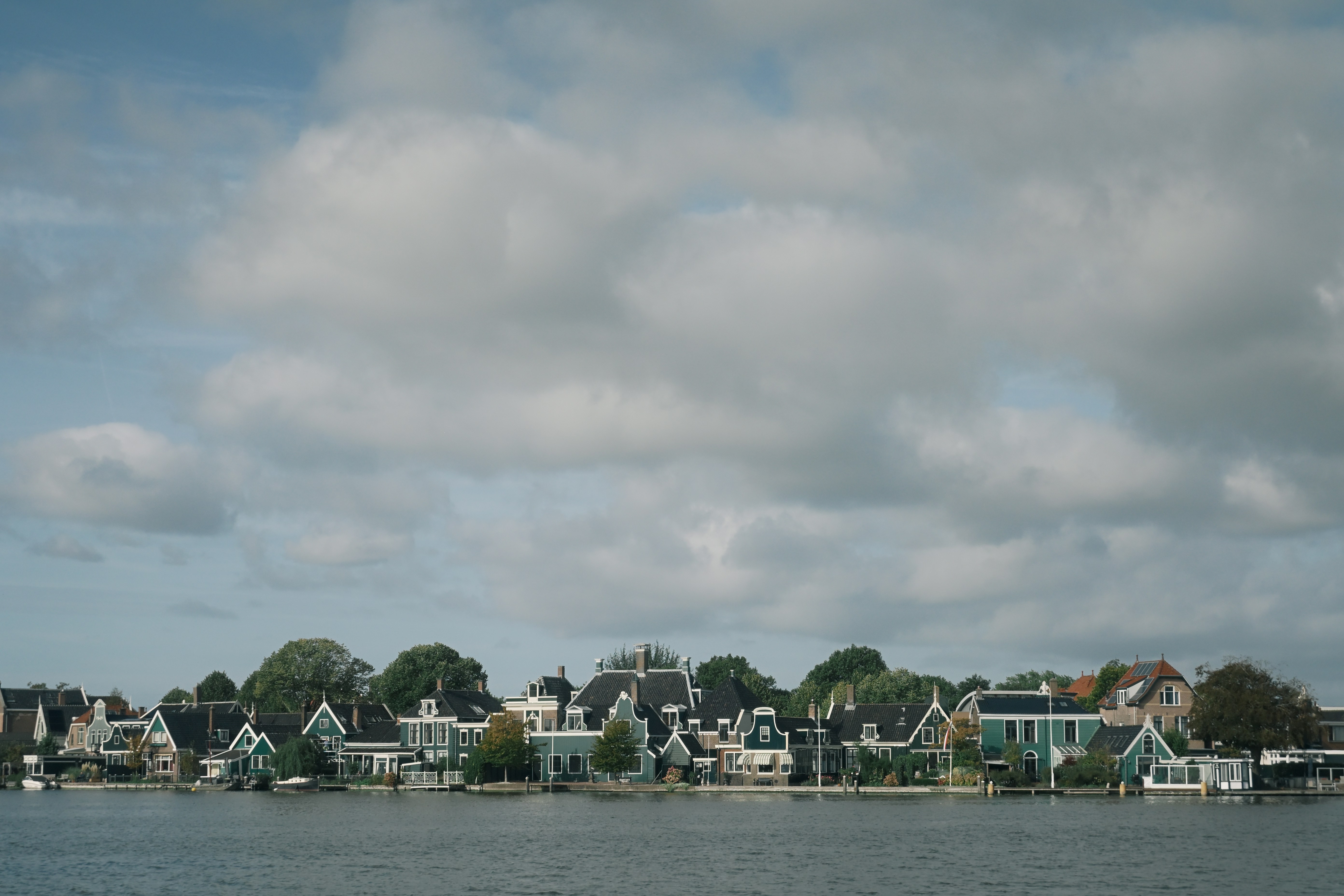 Green houses with white trim along a riverbank under a cloudy blue sky