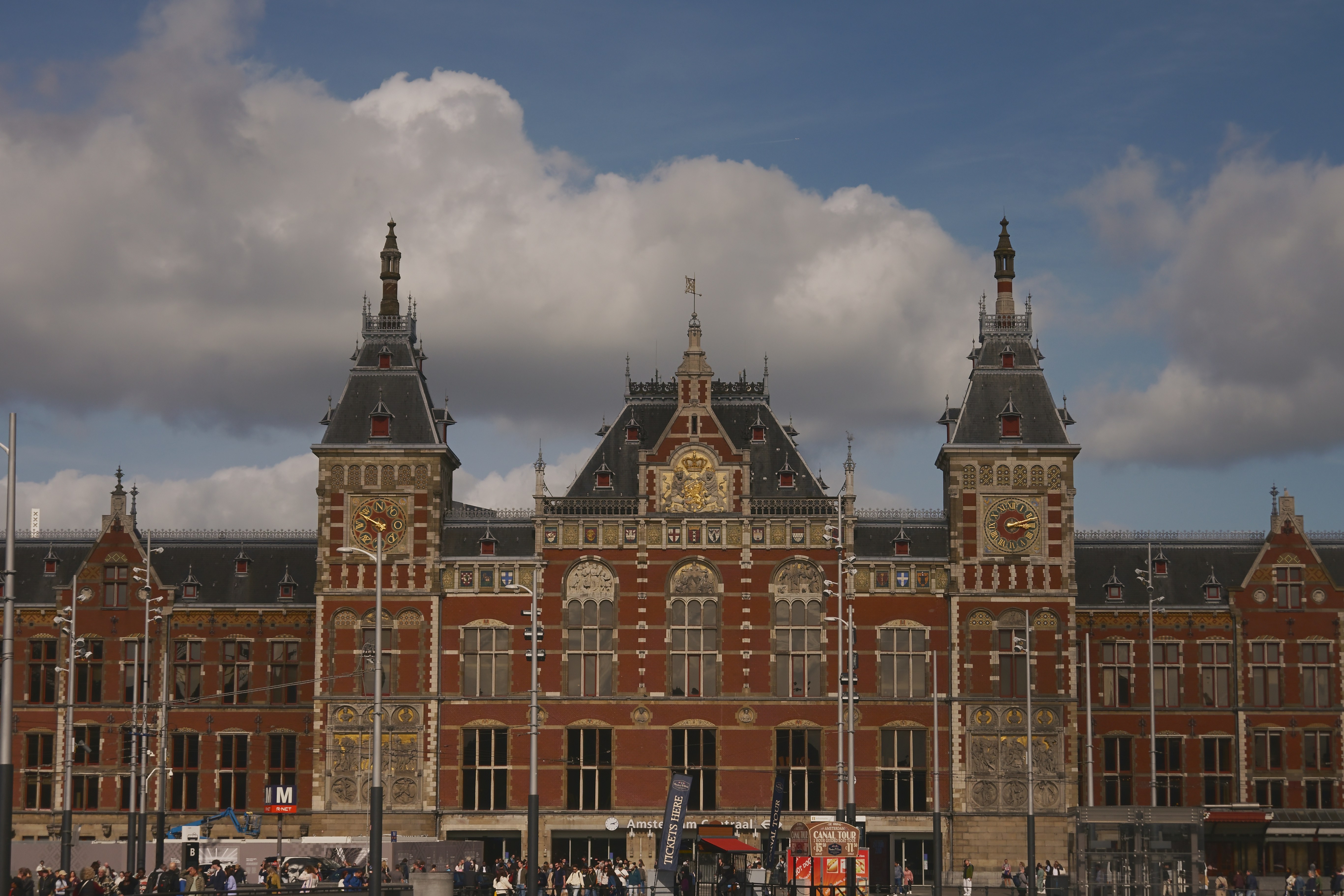 The ornate red brick facade of Amsterdam Centraal railway station under a cloudy sky
