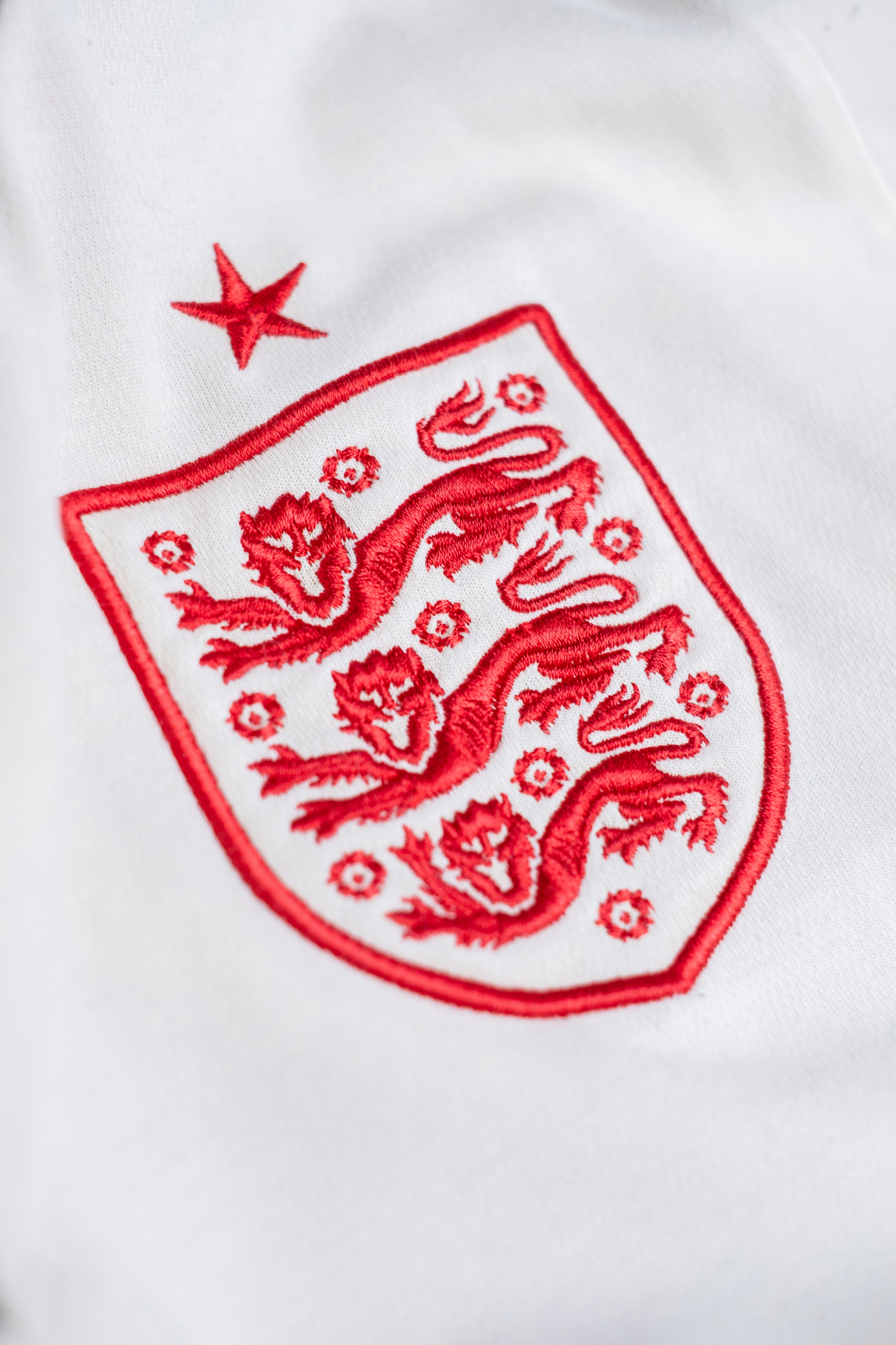 A red embroidered crest with three lions and a star on white fabric