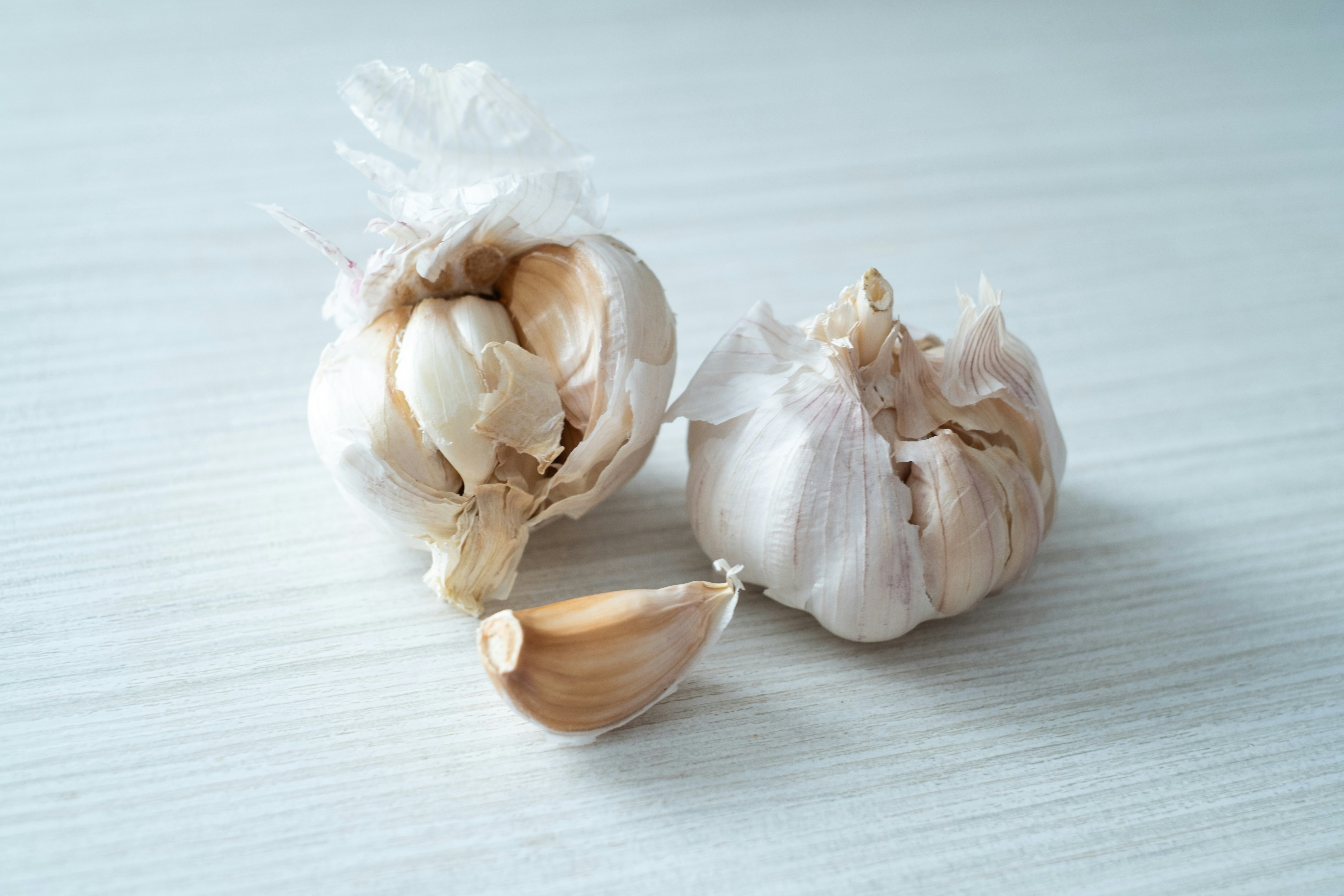 Two whole garlic bulbs and one peeled clove on a light wooden surface