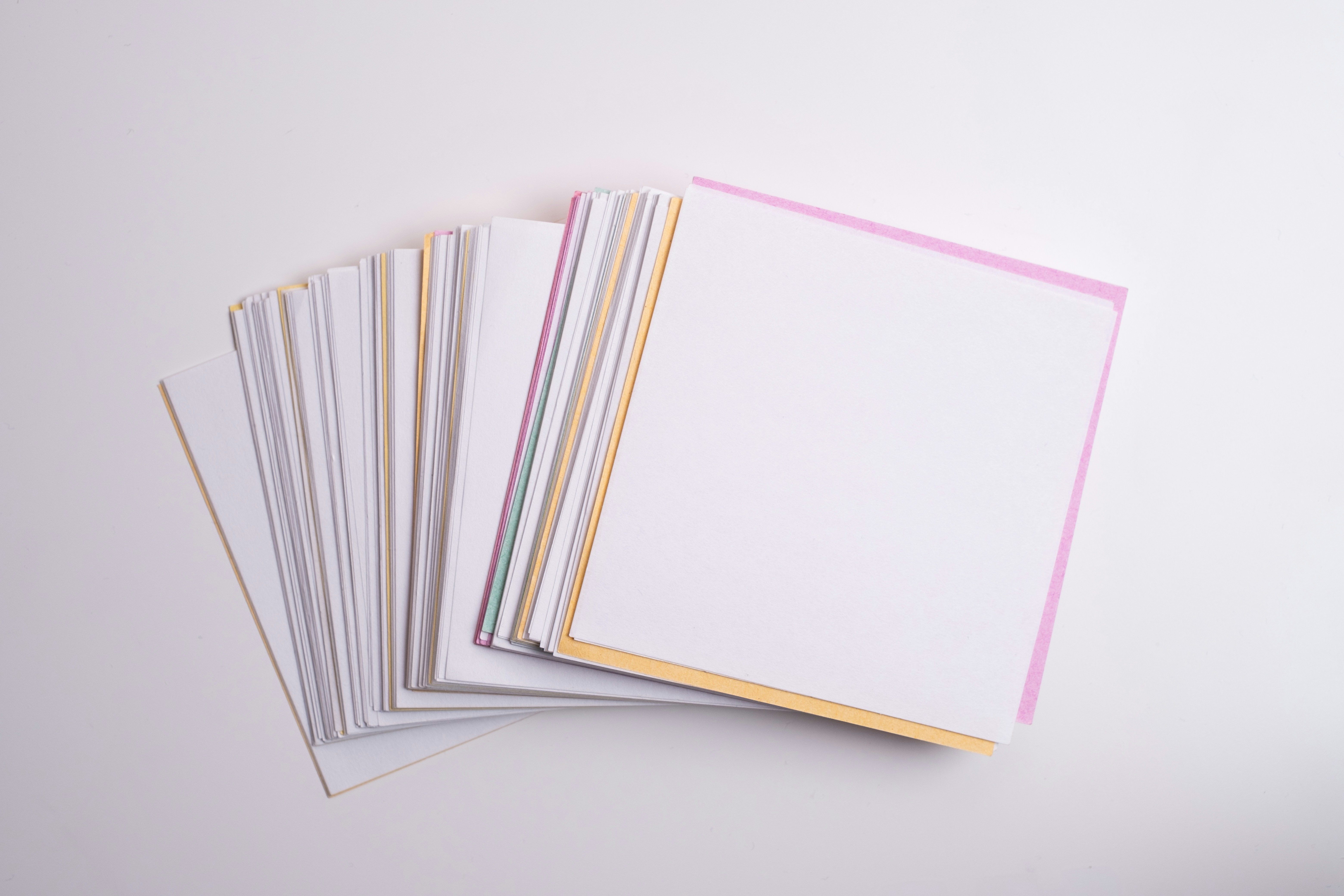 A stack of square paper sheets with colorful edges on a white surface
