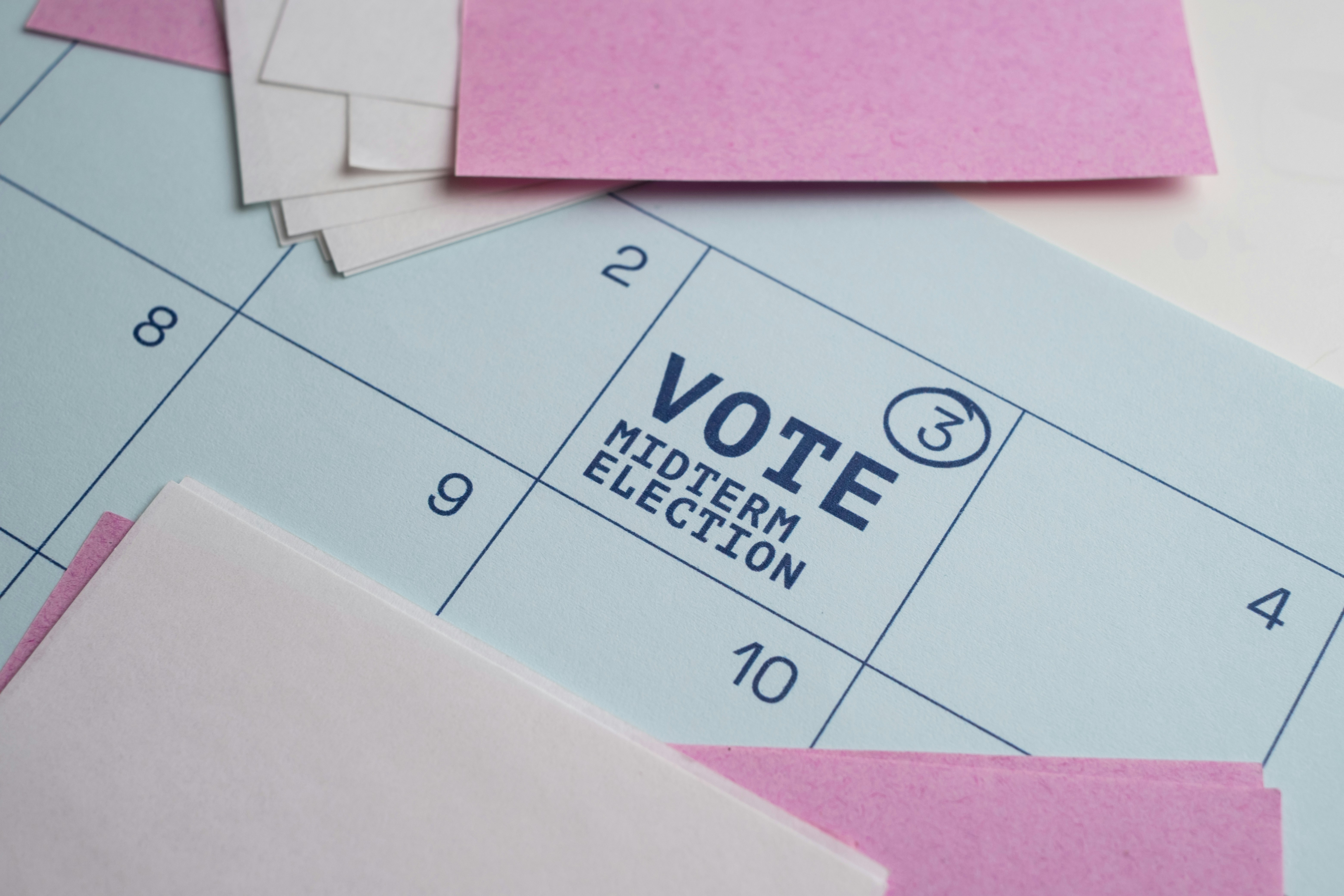 A calendar page with pink paper notes and text reading VOTE MIDTERM ELECTION