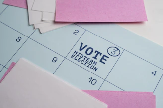 A calendar page with pink paper notes and text reading VOTE MIDTERM ELECTION