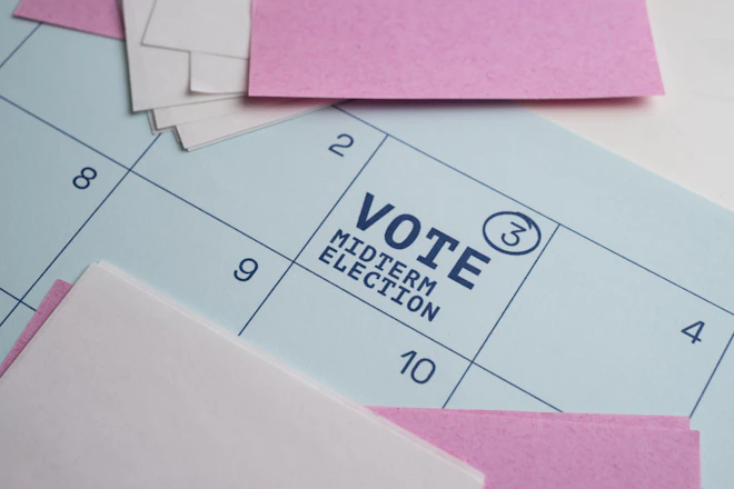 A calendar page with pink paper notes and text reading VOTE MIDTERM ELECTION