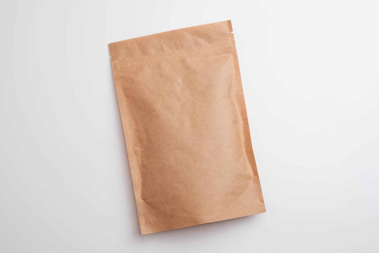 a blank kraft-paper coffee bag lying flat on a white table