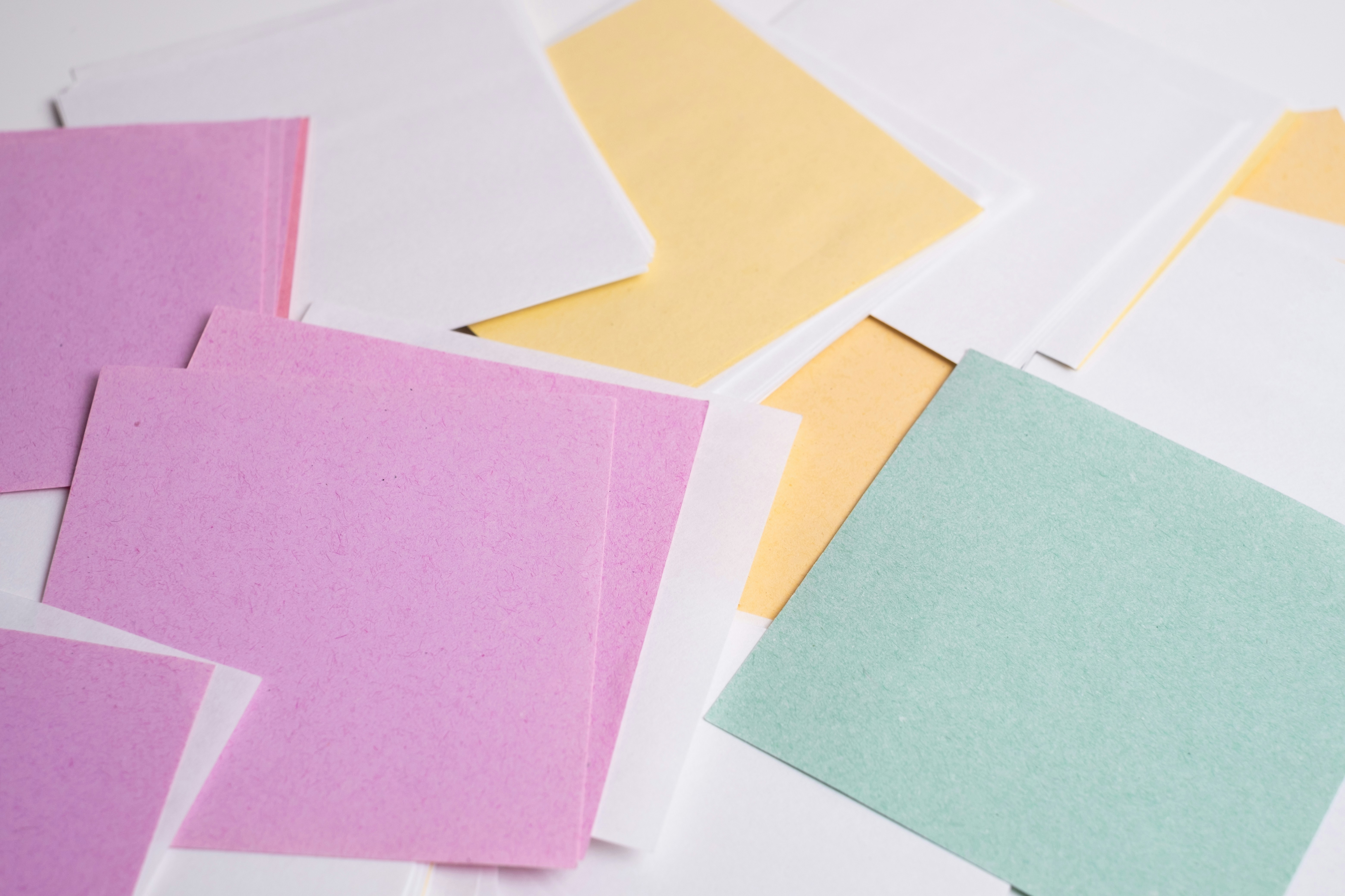 A scattered pile of pastel pink, yellow, and mint green paper sheets