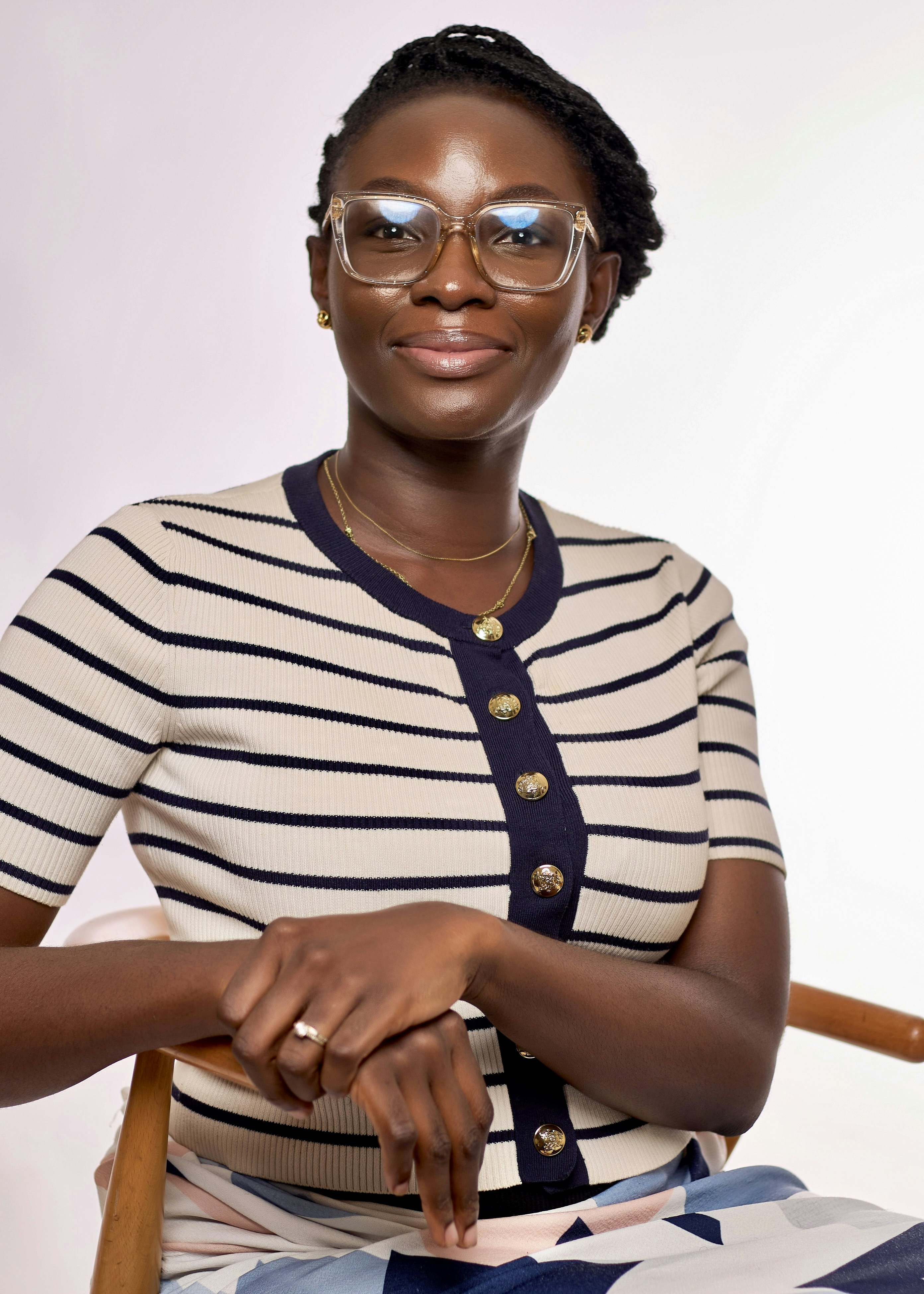 A woman wearing clear-framed glasses and a striped cardigan with gold buttons