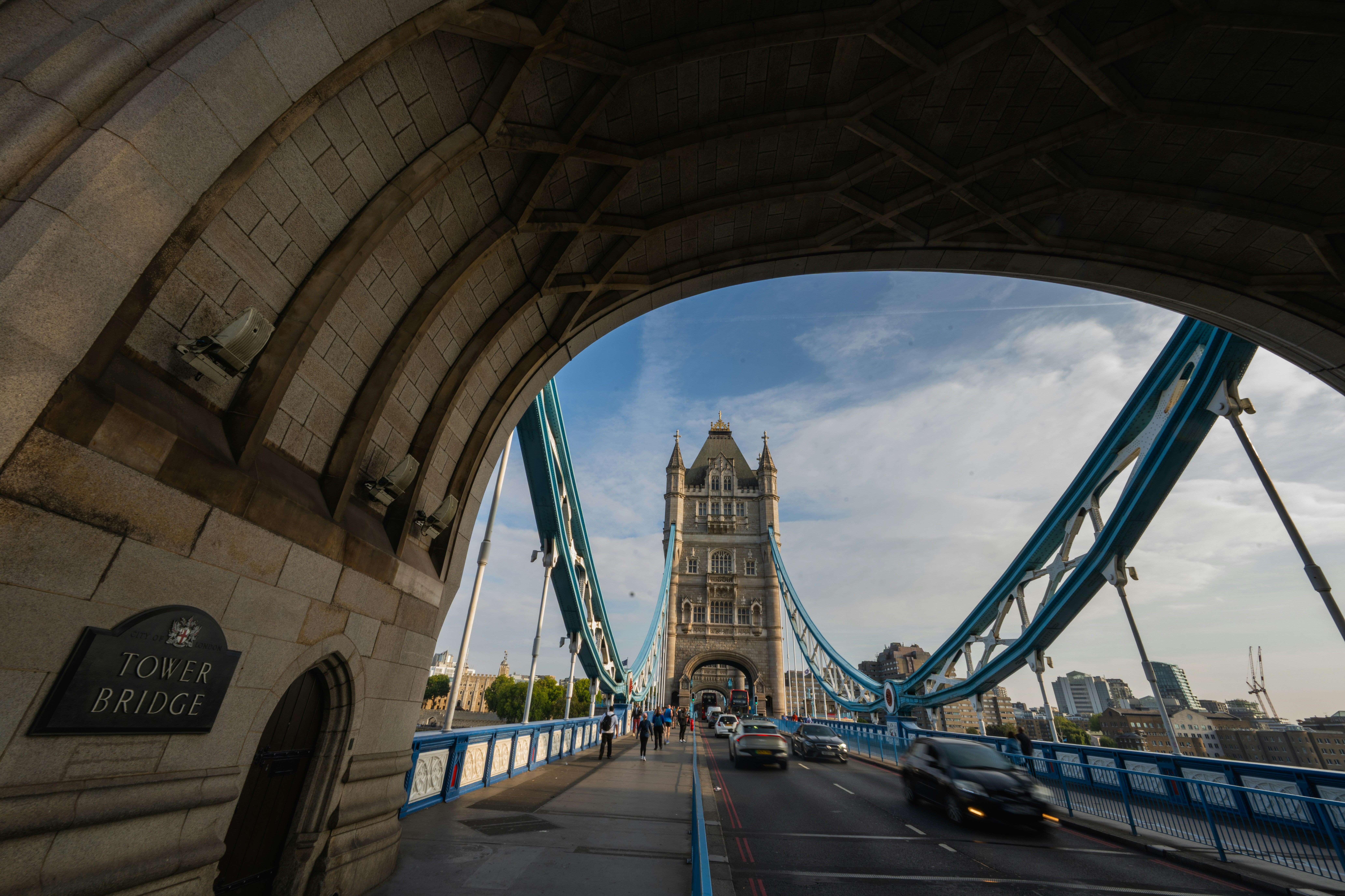 Cars driving across Tower Bridge in London under a blue sky with clouds