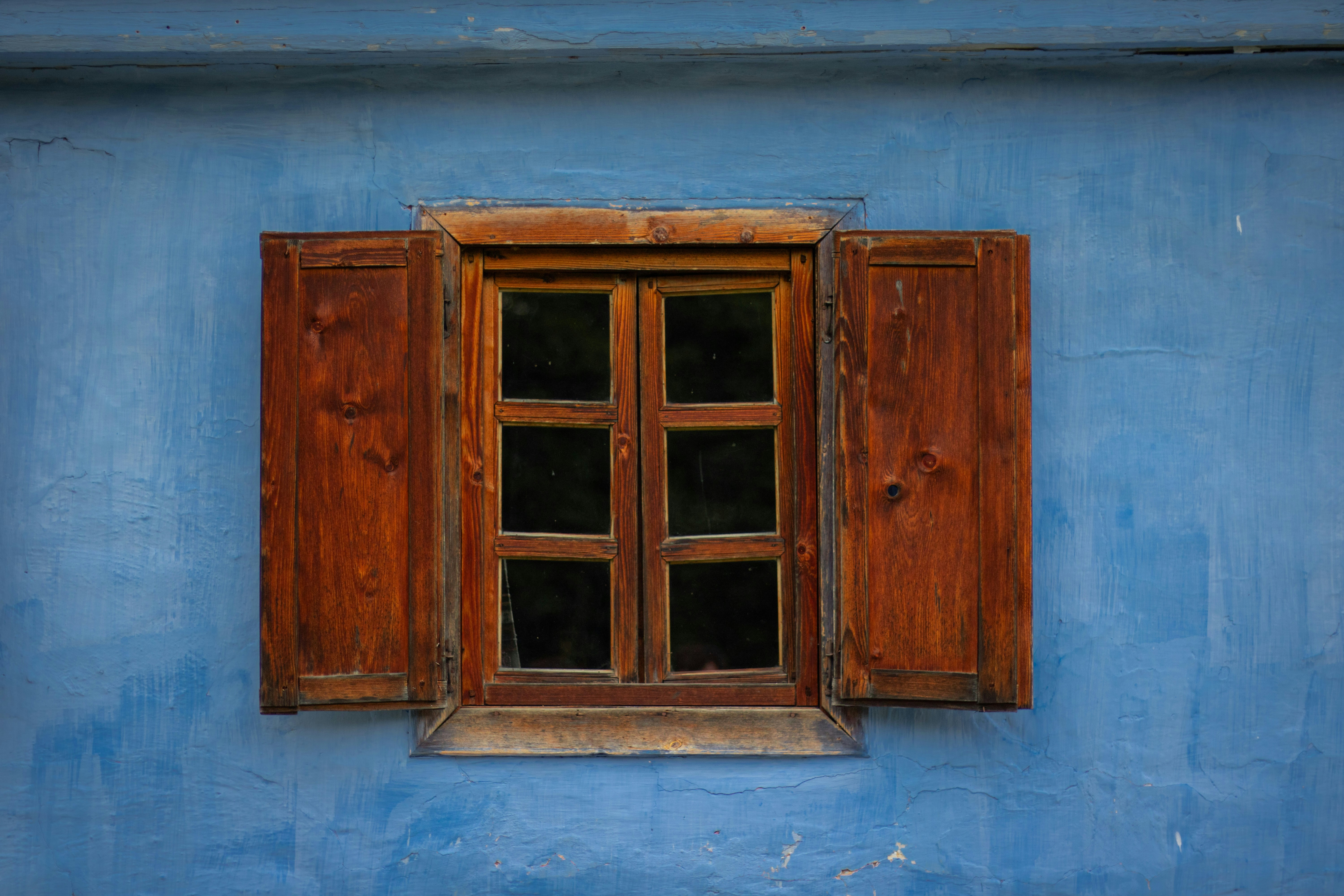 A wooden window with open shutters set into a textured blue wall