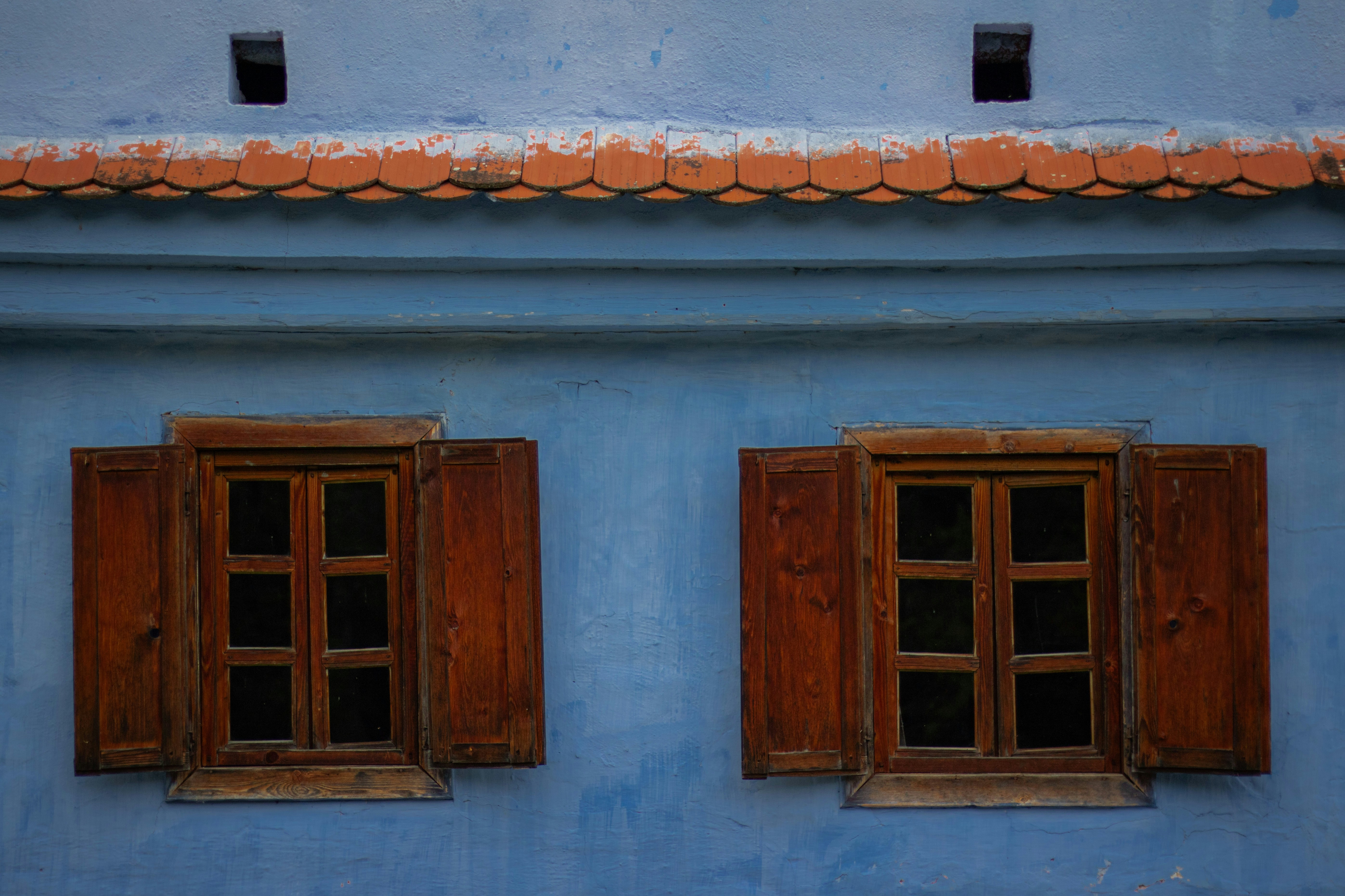 Two wooden windows with open shutters on a bright blue plaster wall