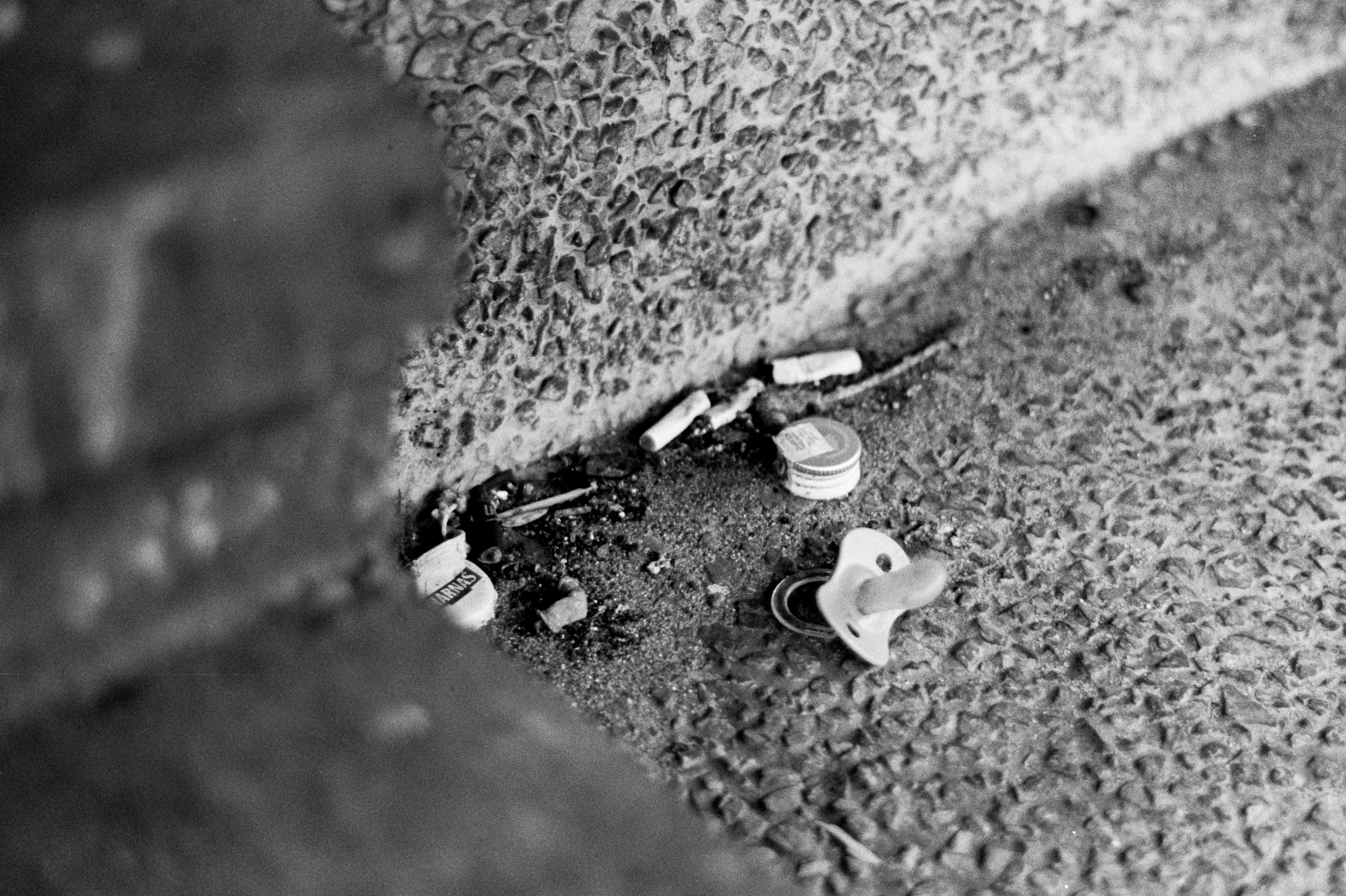 A baby pacifier, cigarette butts, and bottle caps on a textured concrete surface
