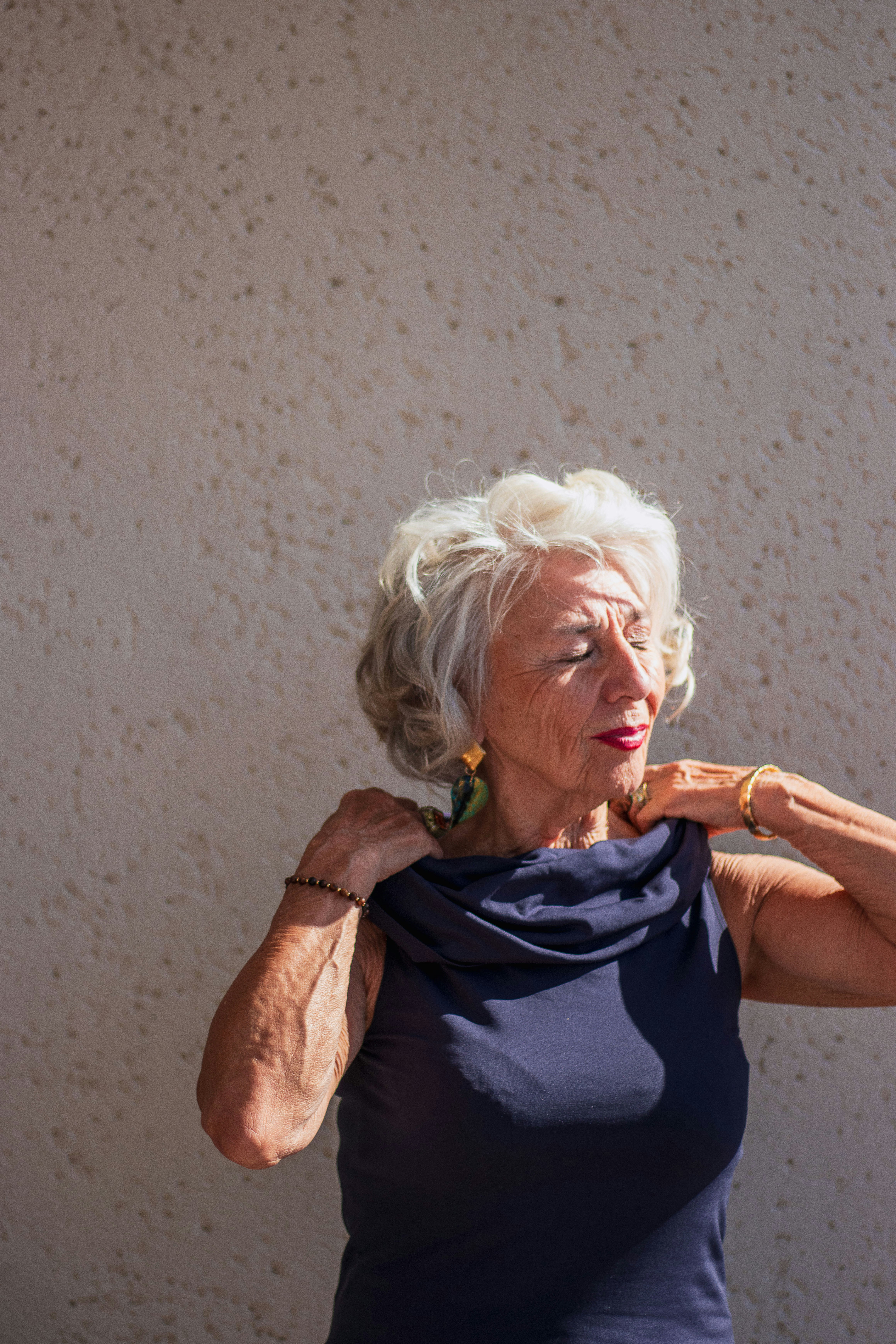 An older woman with white hair adjusting her dark blue sleeveless top