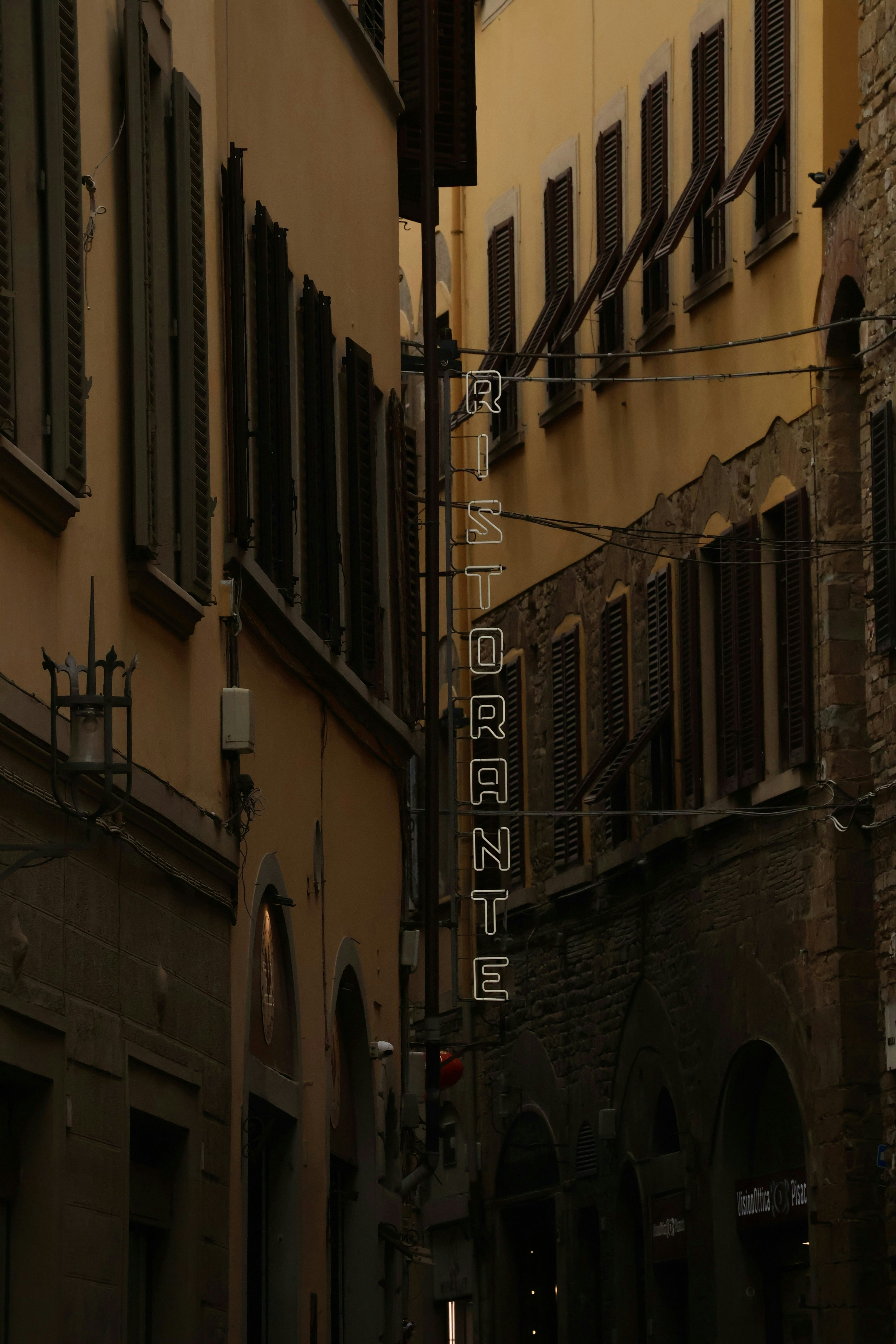 A vertical neon sign reading RISTORANTE in a narrow alleyway between old buildings