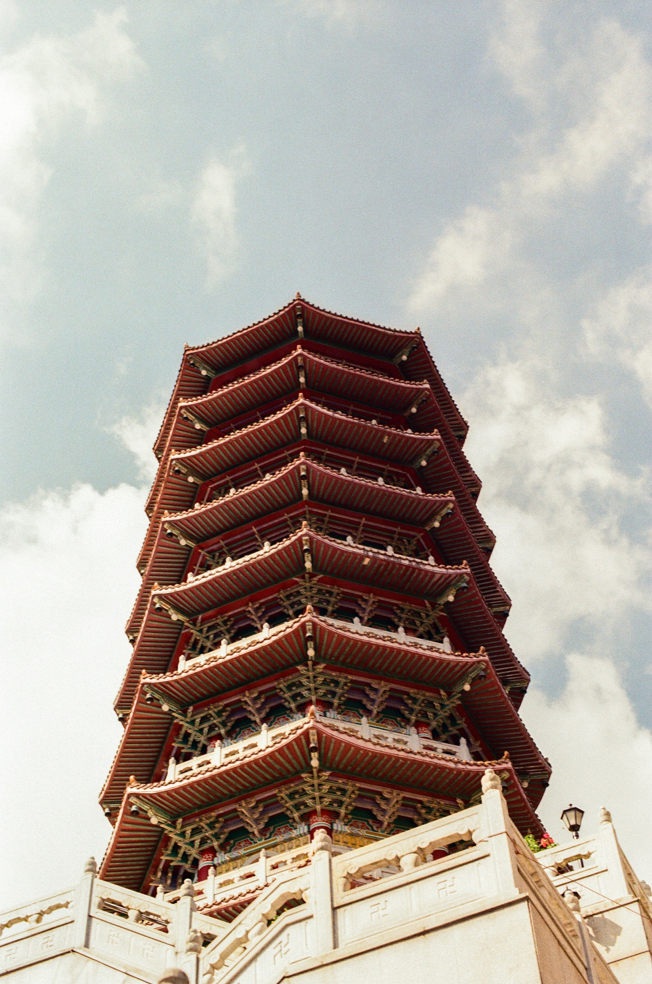 A multi-tiered red pagoda tower against a blue sky with scattered white clouds