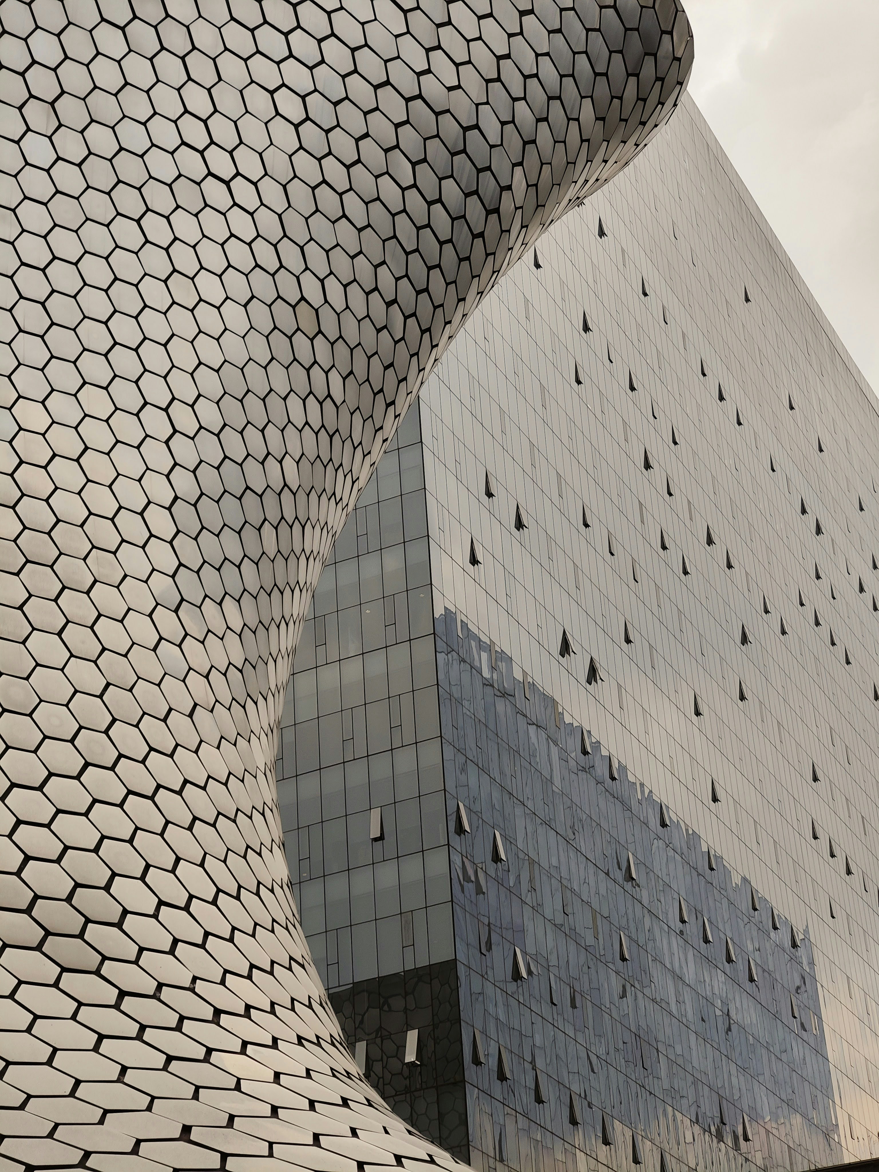 A curved facade with hexagonal tiles beside a glass skyscraper with small open windows