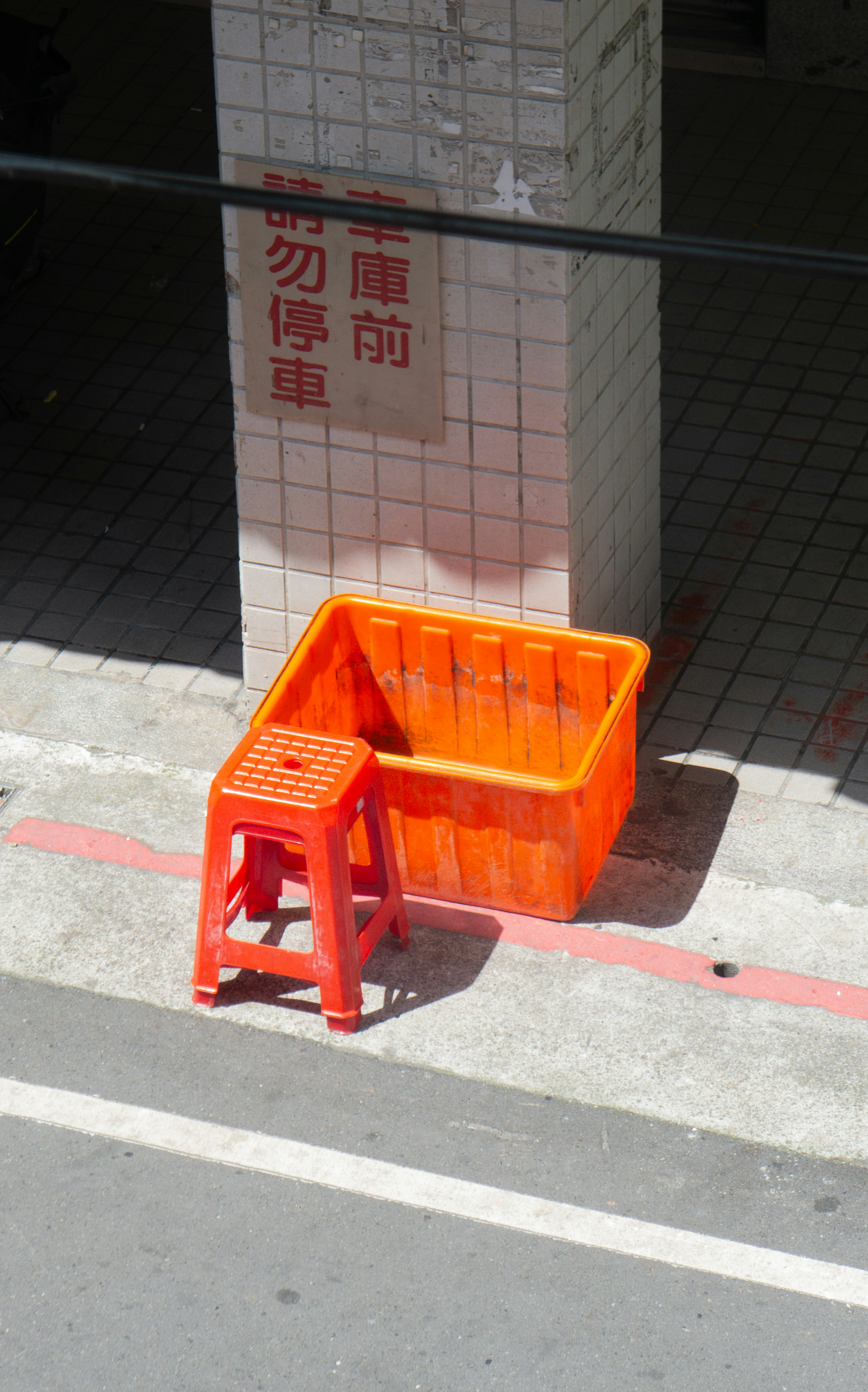 An orange plastic crate and a matching stool on a sidewalk by a pillar