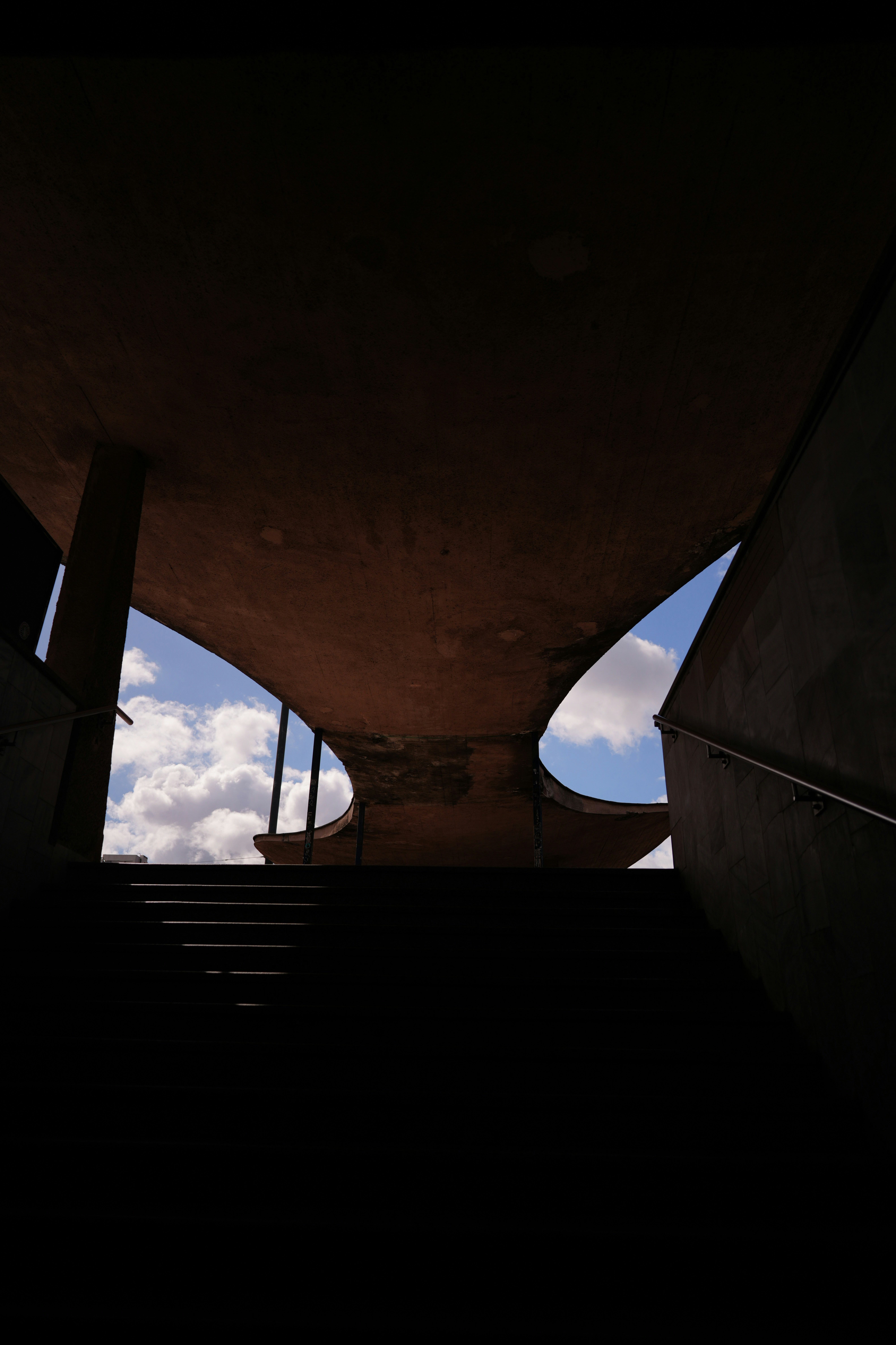 Concrete staircase leading up to a curved architectural canopy against a blue sky