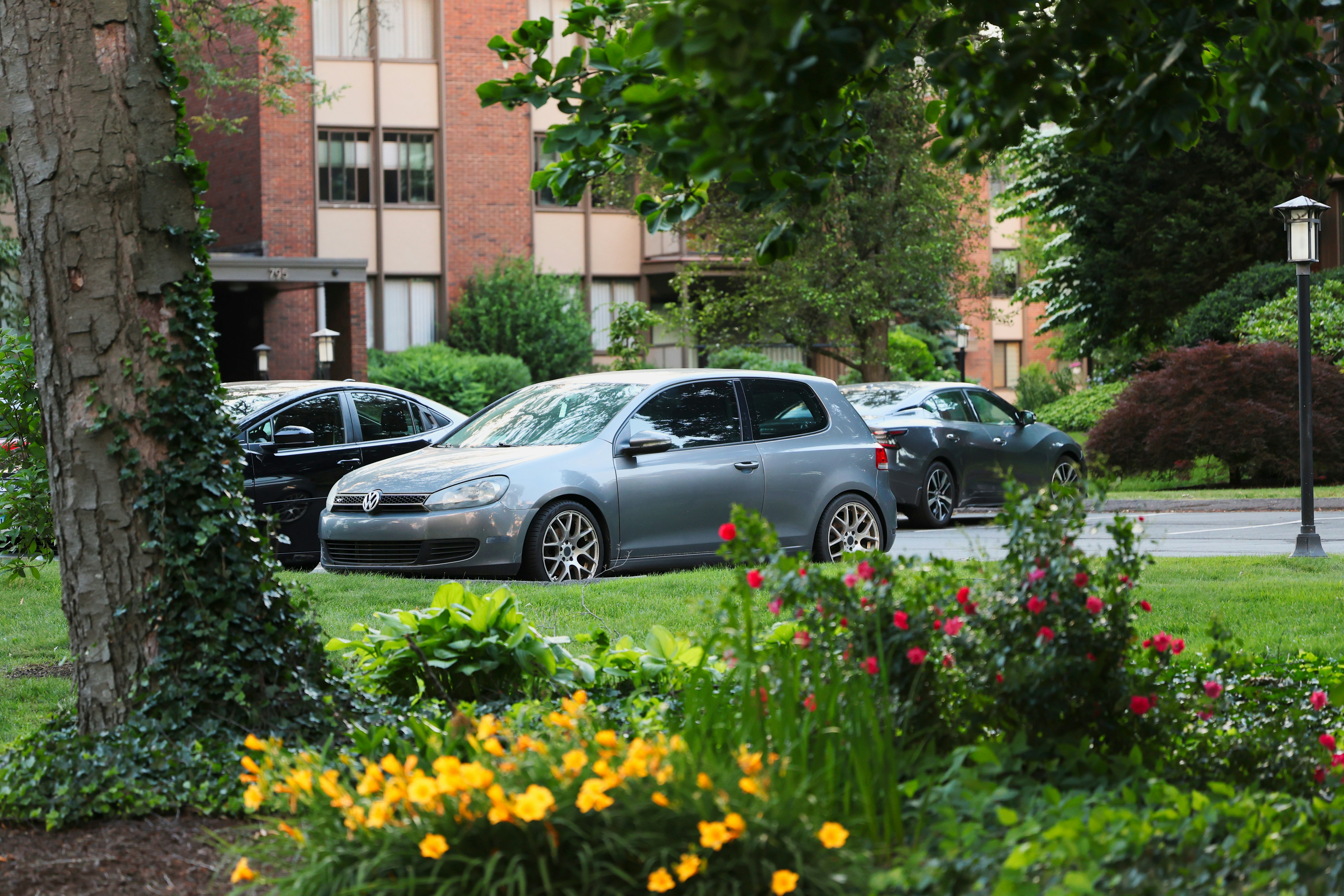 A grey hatchback parked on a grassy lawn near a brick apartment building