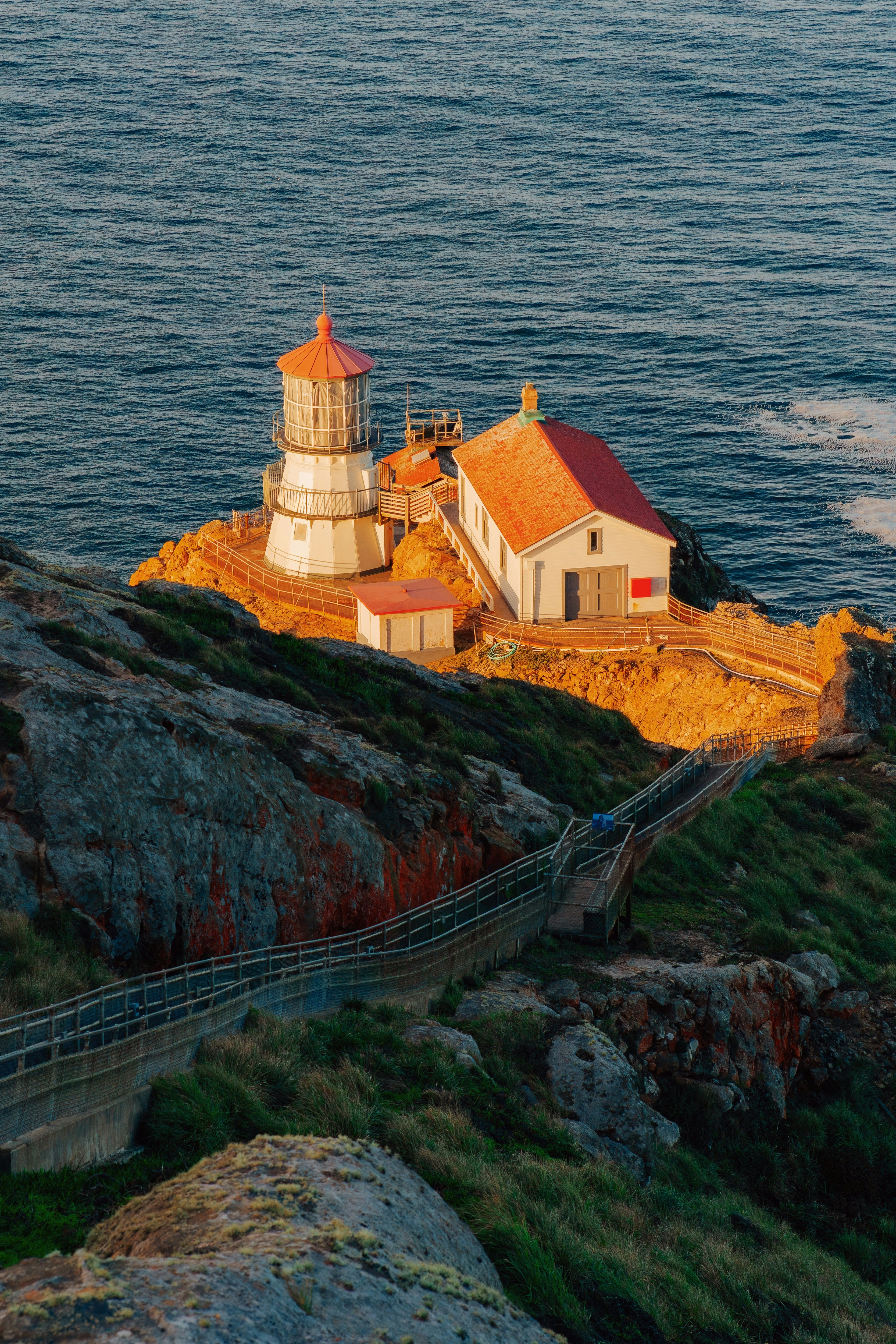 A lighthouse with a red roof on a rocky cliff above the ocean