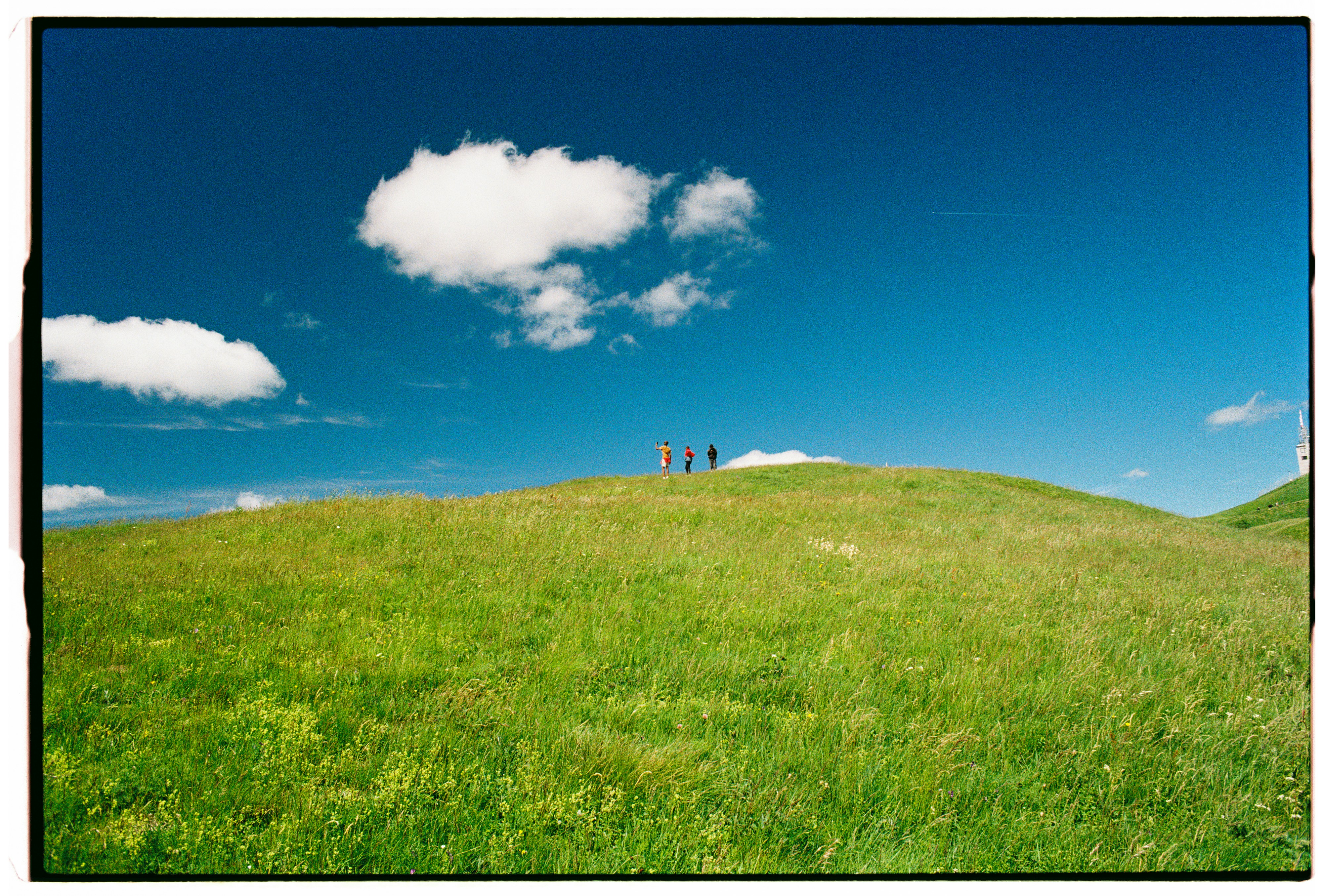 Three people standing on a grassy hill under a bright blue sky
