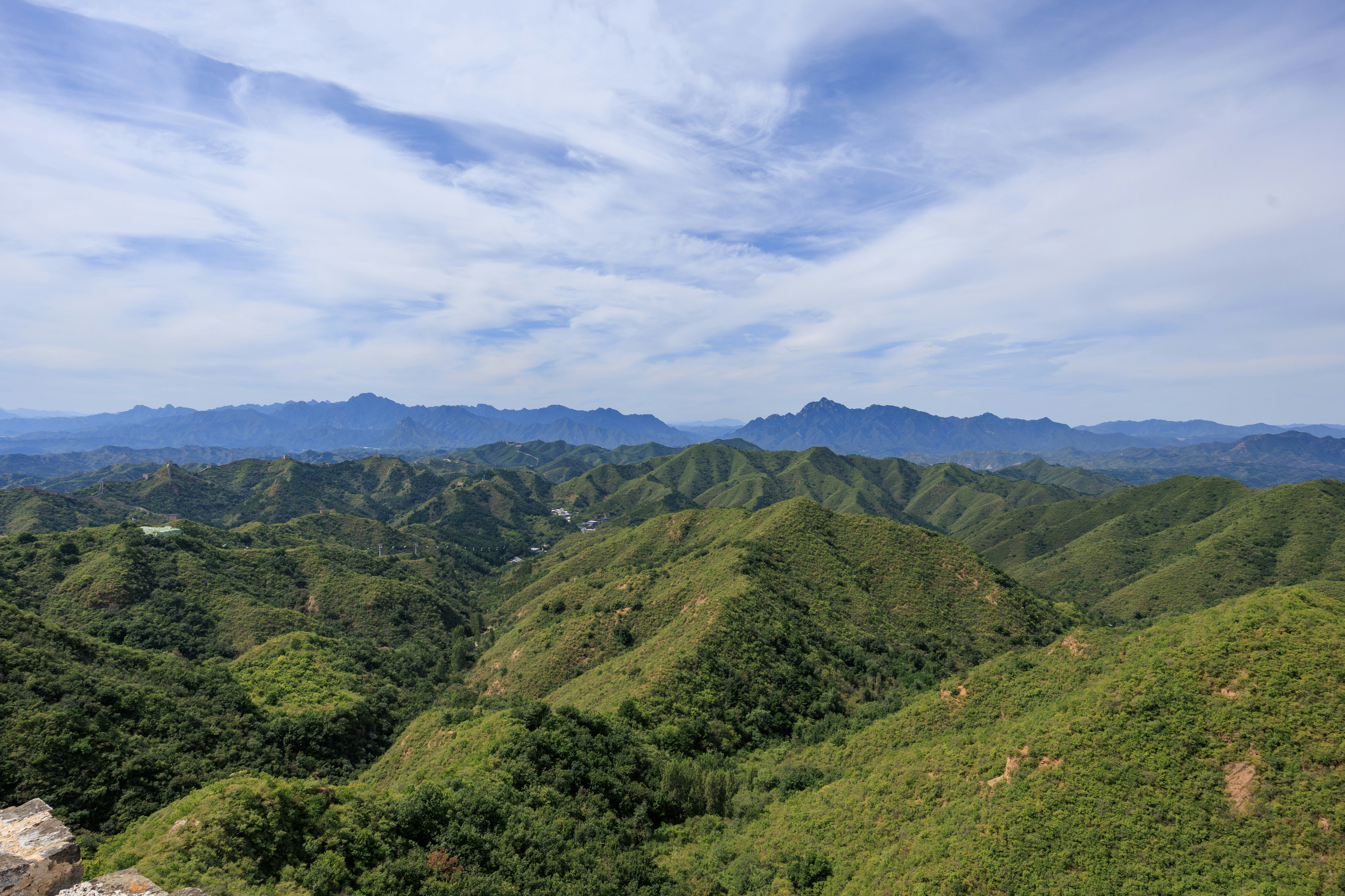 Green rolling mountains under a blue sky with wispy white clouds
