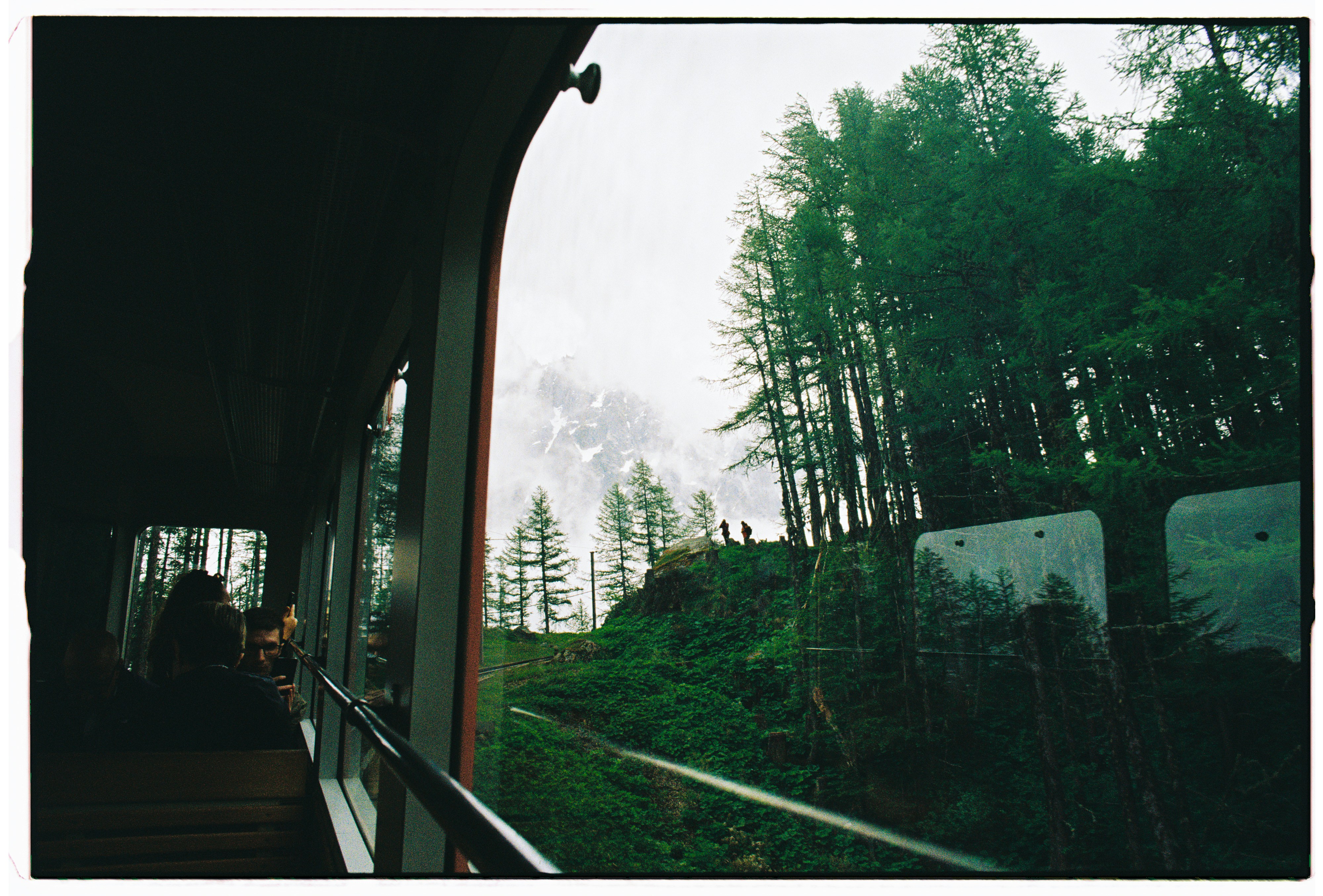 View from a train window of a forested mountain slope and misty peaks