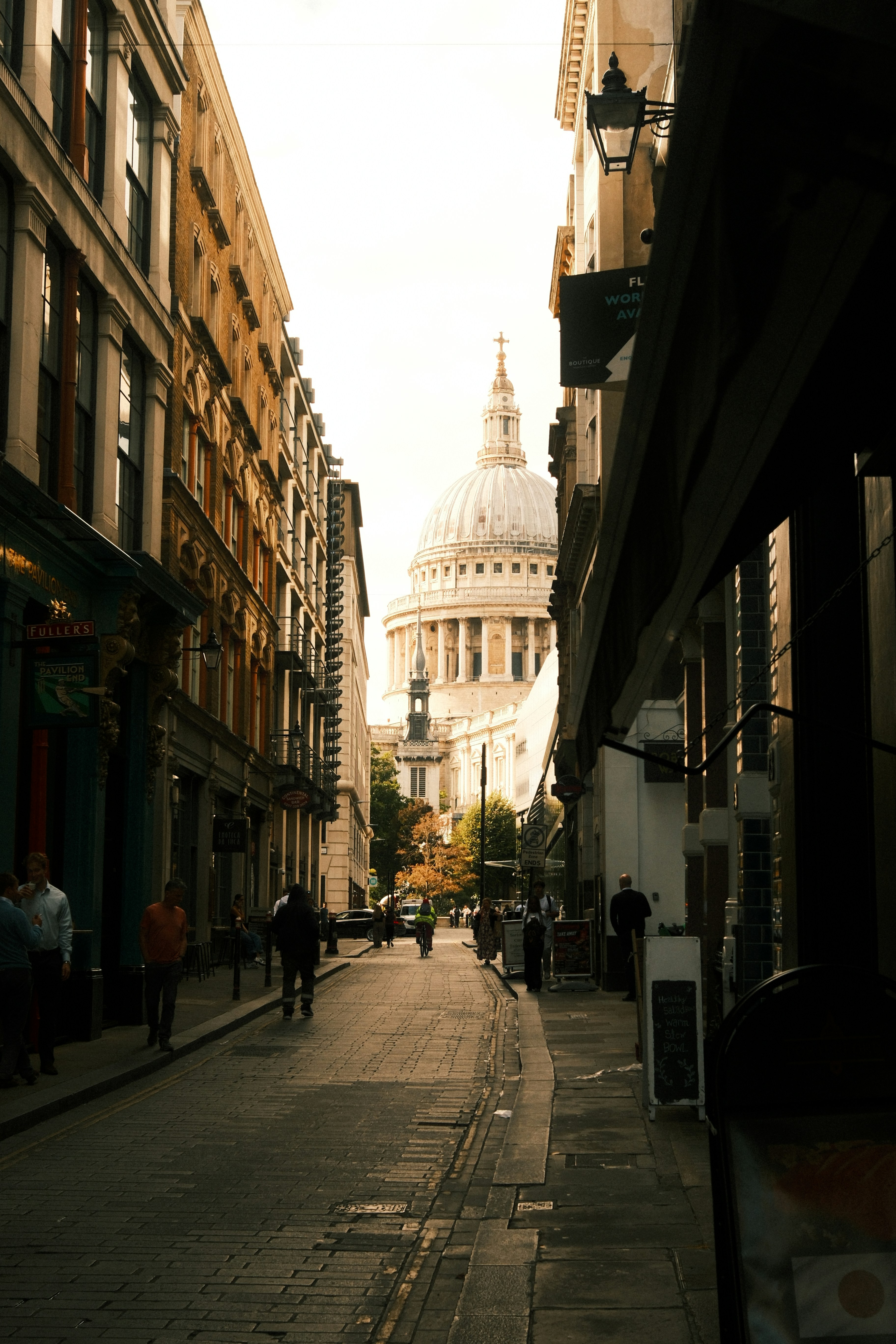 People walking on a cobblestone street toward St Paul's Cathedral in London