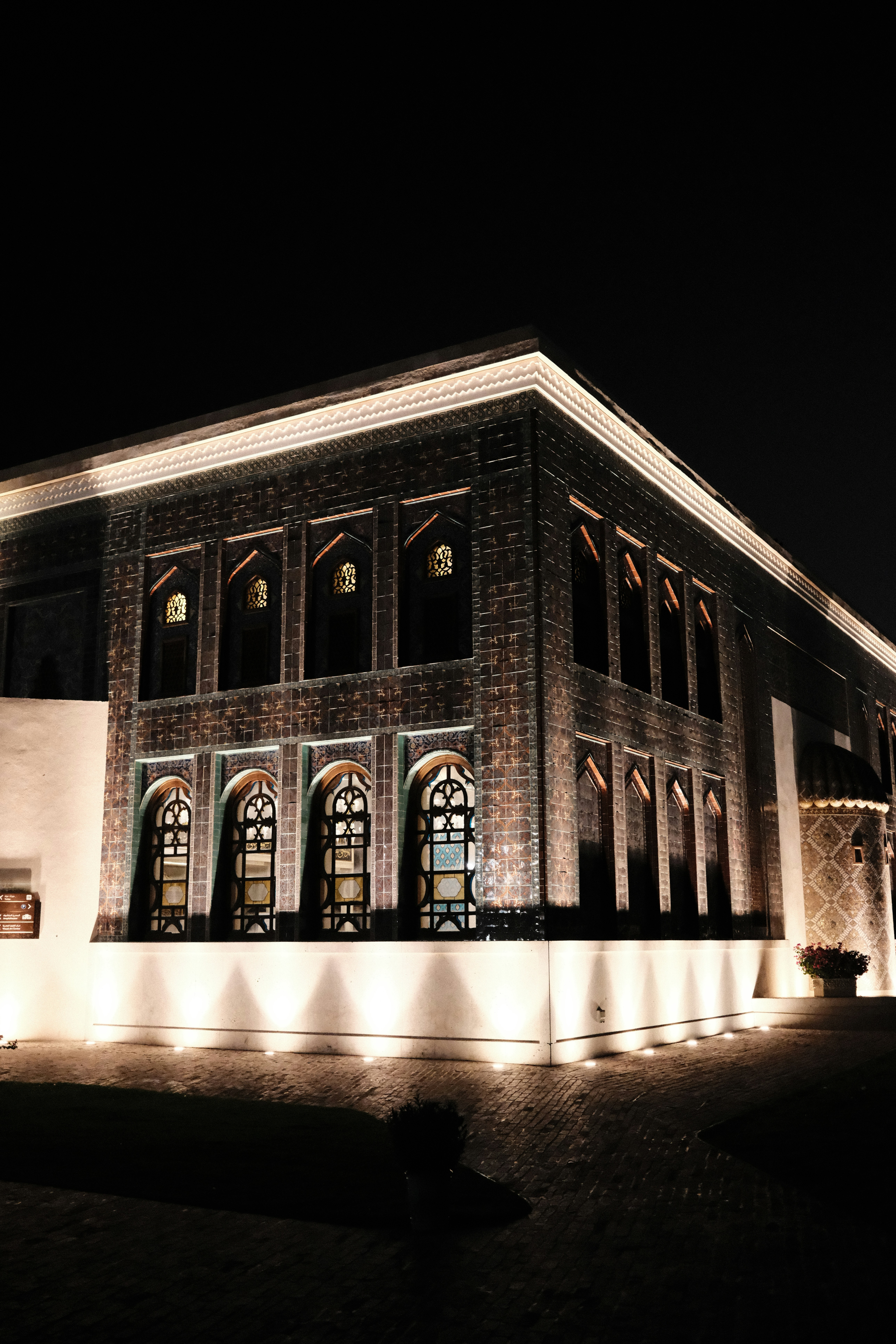 A tiled building with arched windows illuminated by warm ground lights at night