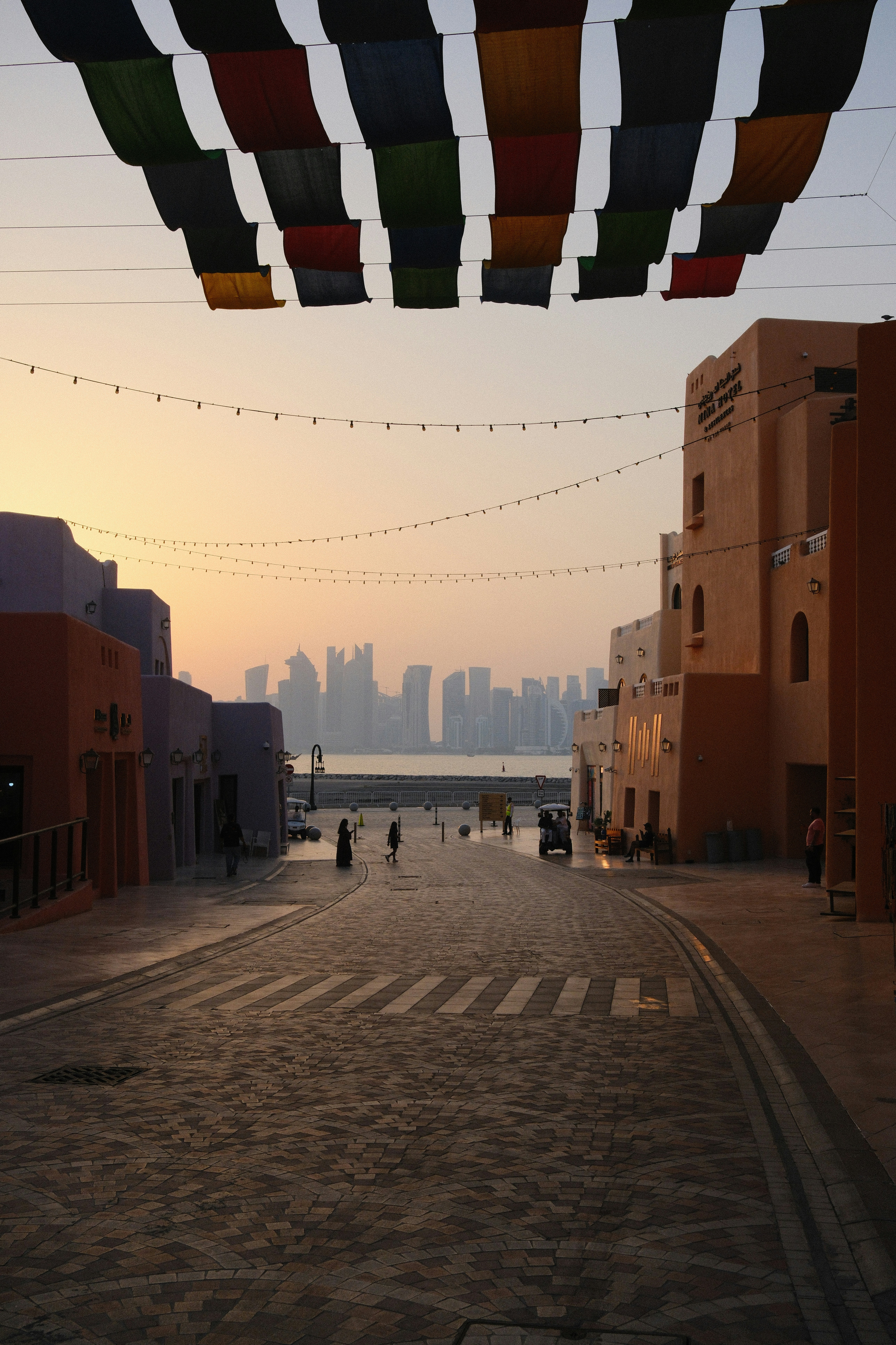 People walking on a cobblestone street under colorful flags with a distant city skyline
