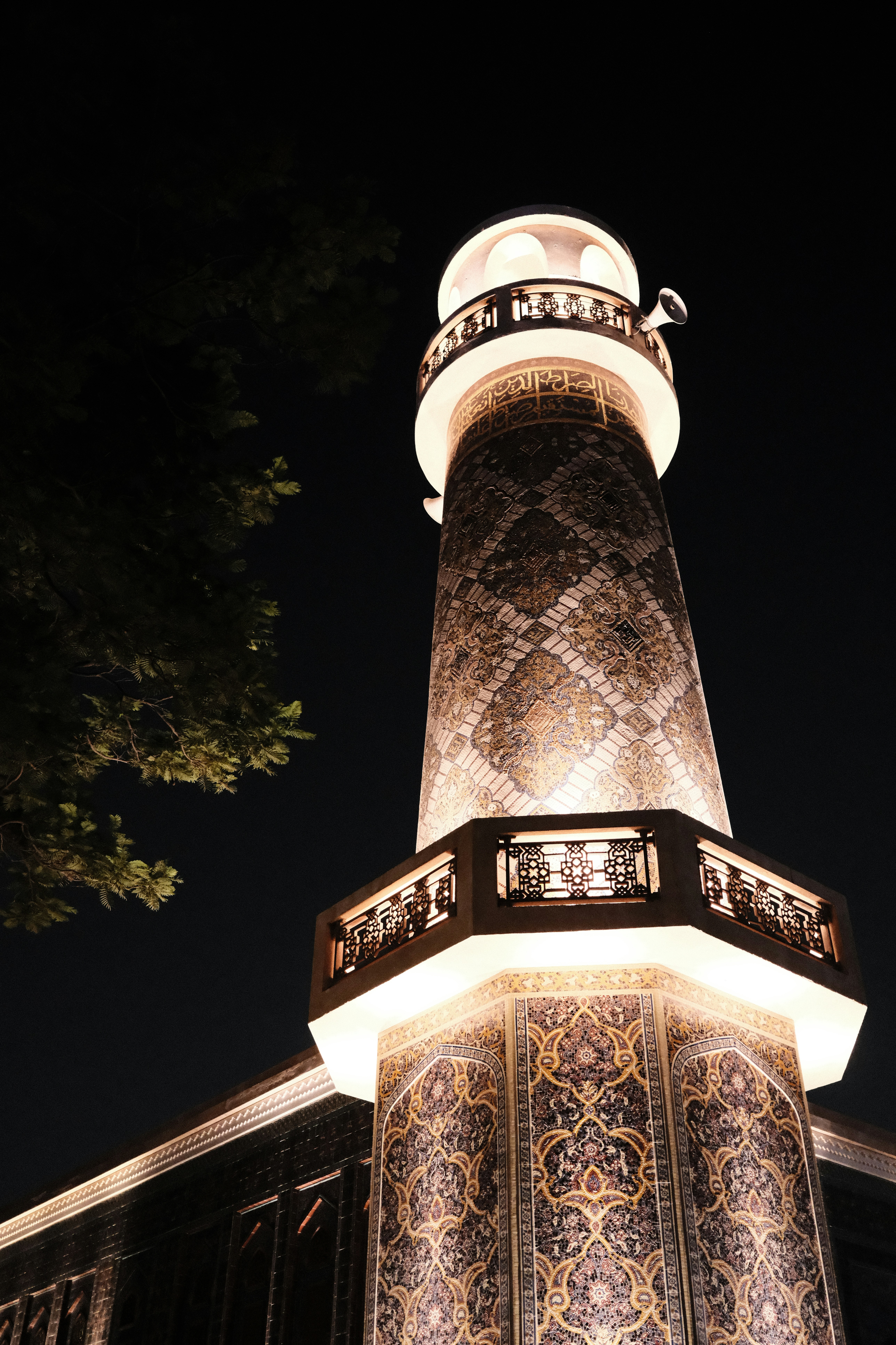 An illuminated minaret with intricate tile patterns against a dark night sky